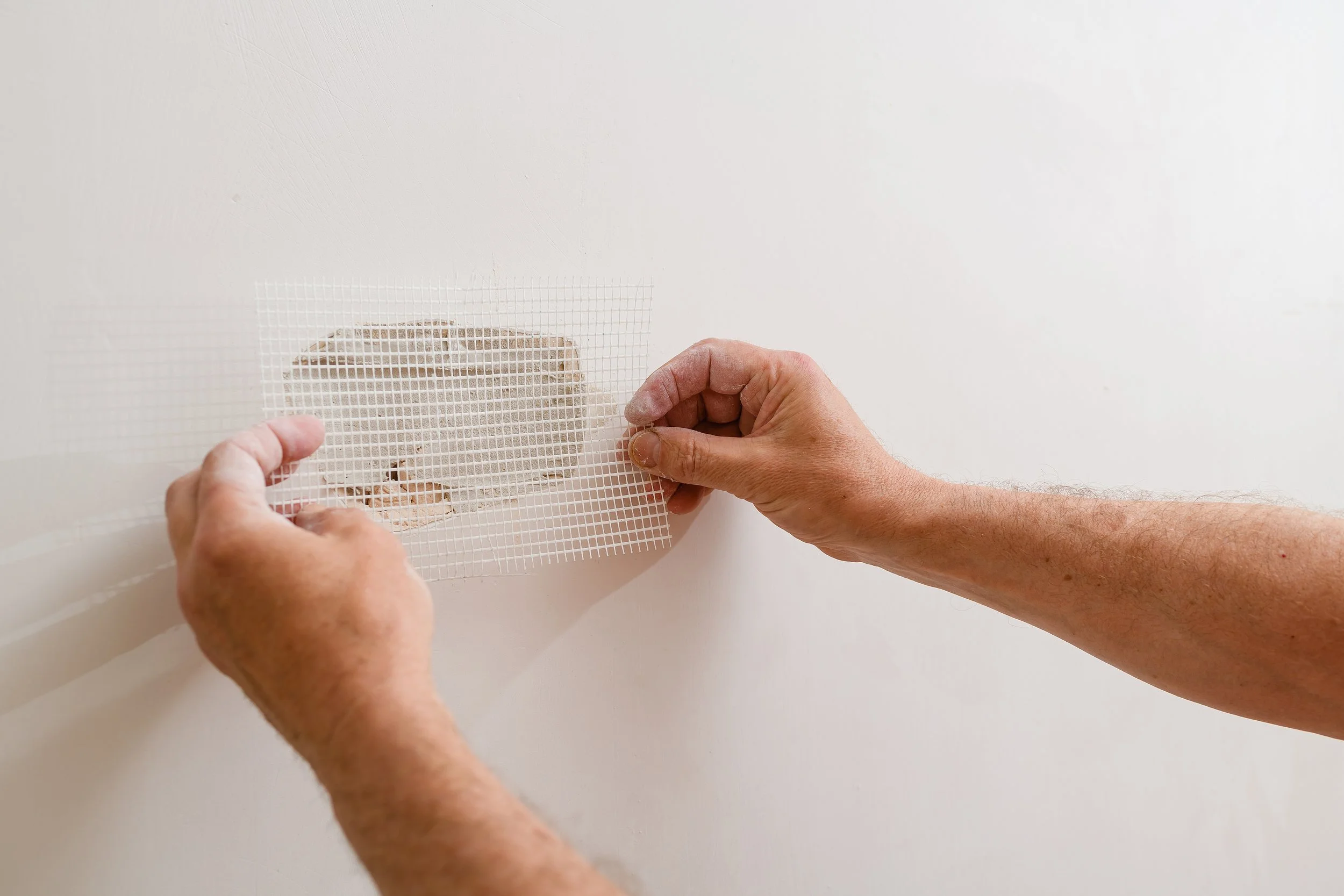Person applying mesh drywall tape over a wall hole