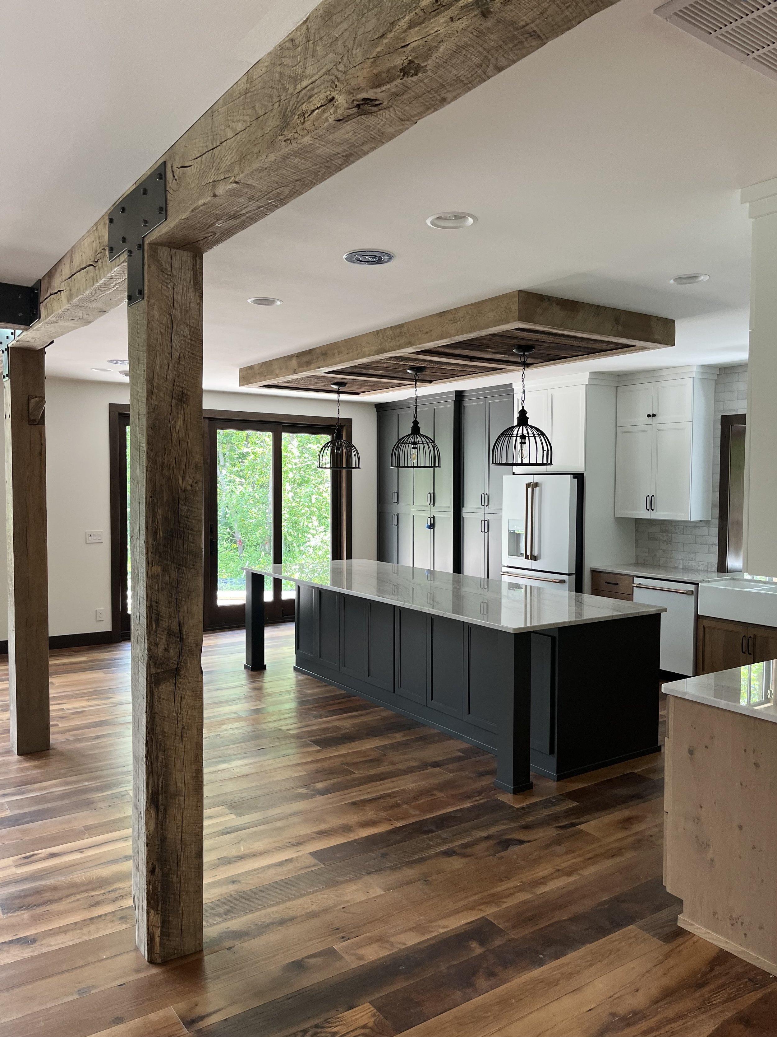 Modern kitchen with a large island, white and gray cabinets, wooden accents, pendant lights, and hardwood flooring.