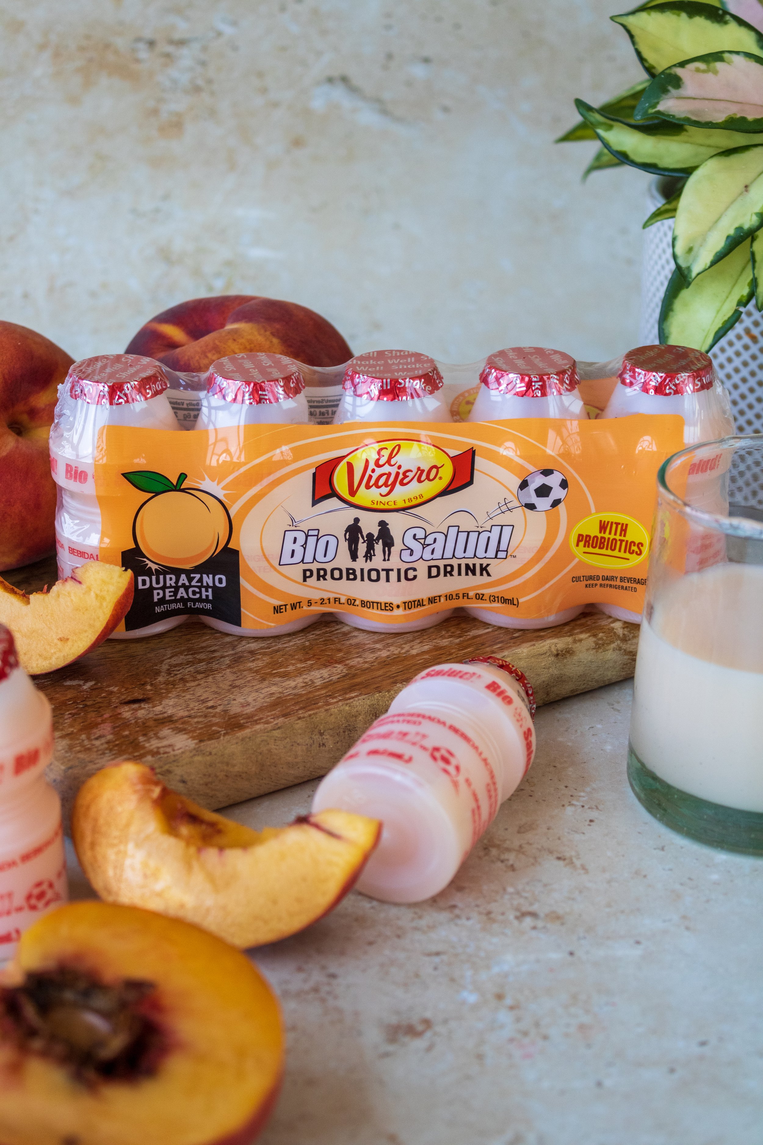A pack of El Viajero Bio Salud probiotic drinks, with peaches and a glass of yogurt on a kitchen counter.