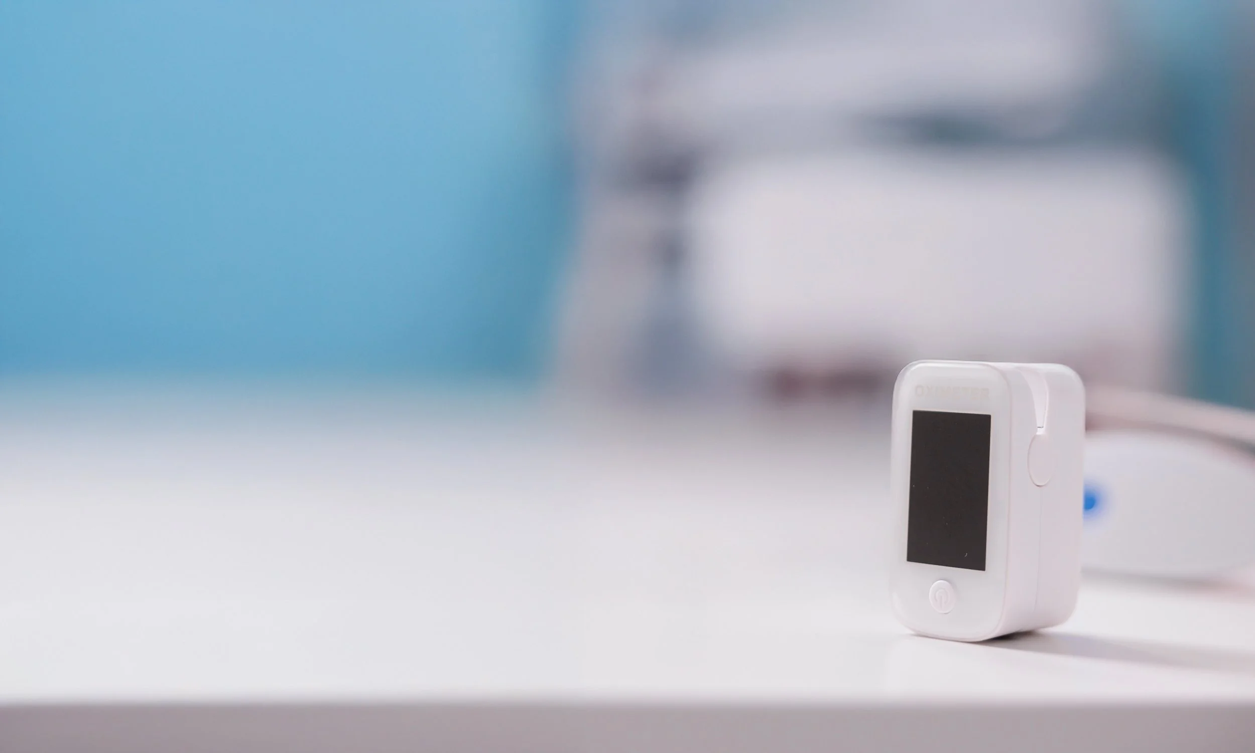 oximeter in white colour, sitting on a clean with blue and white background, one of the medical devices
