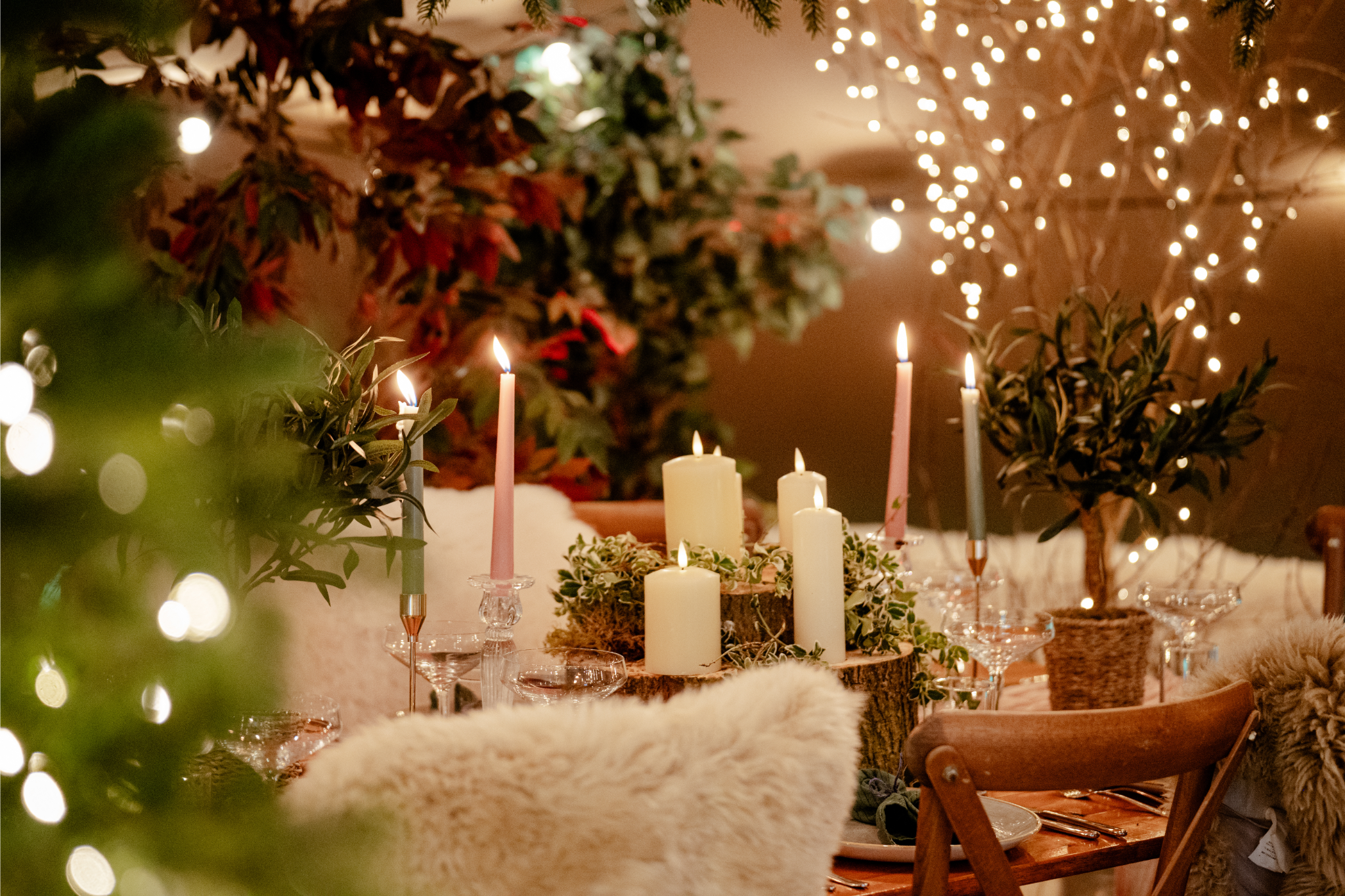A warmly decorated dining table with lit candles, greenery, and fairy lights, set for a cozy holiday gathering.