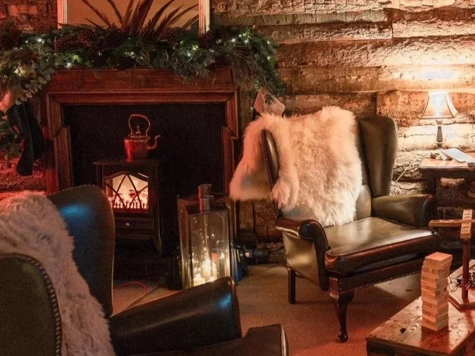 Interior of a decorated bar or restaurant with festive Christmas lights and green garland on the ceiling and around the bar area, with warm lighting and cozy decor.