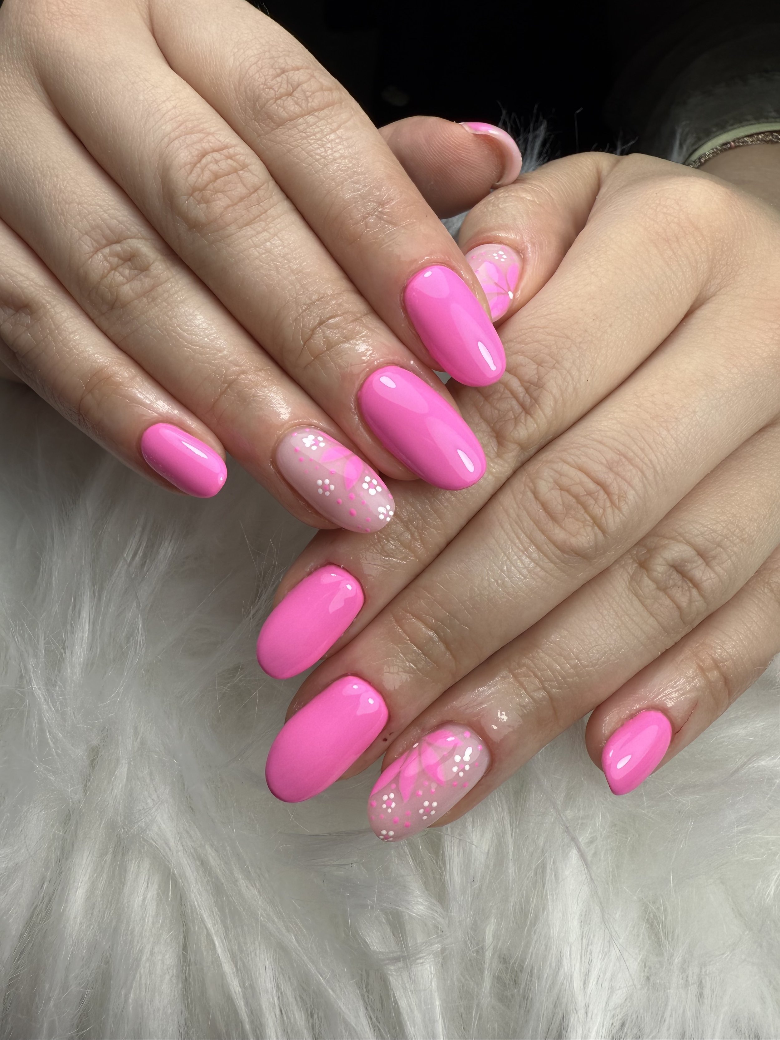 Mains avec vernis à ongles rose et motifs floraux sur un fond blanc duveteux.