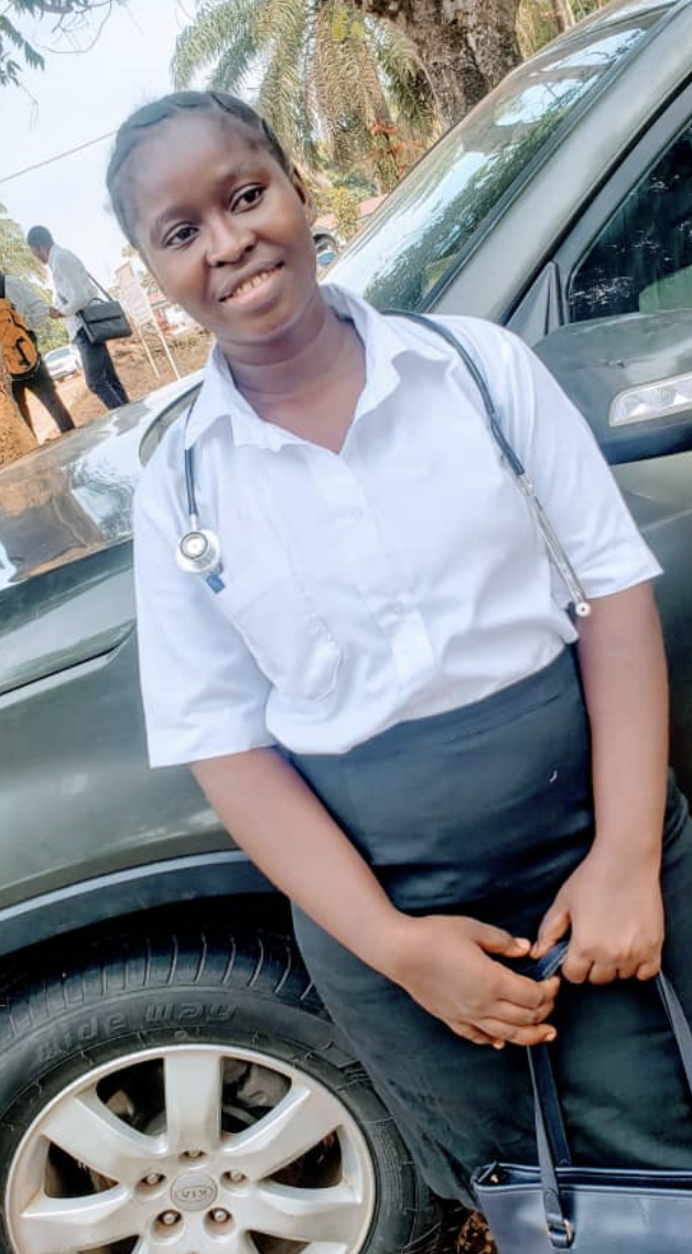 A young woman in a white shirt and black skirt standing outdoors next to a green car, with a stethoscope around her neck and a smiling expression.