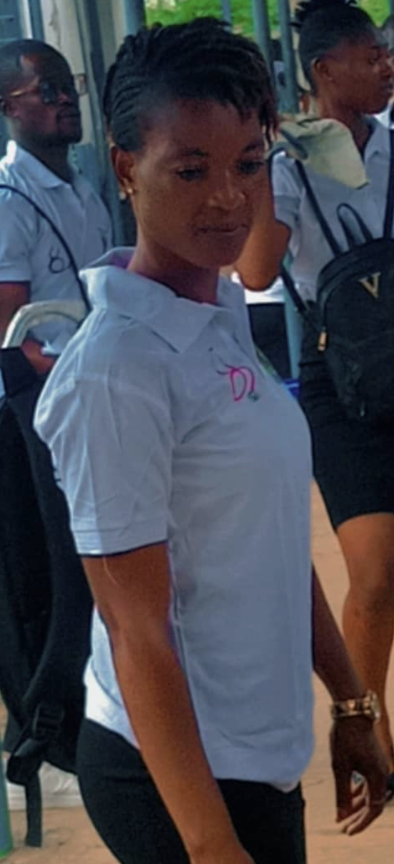 A woman in a white polo shirt with pink embroidered initials, standing outdoors with two other people in similar shirts in the background.