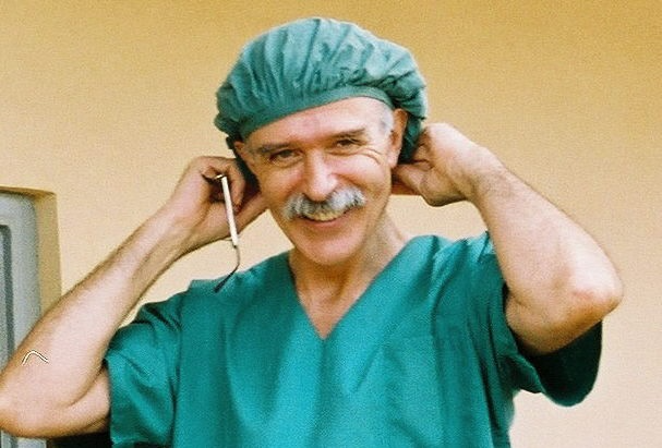 A smiling man in green scrubs and a surgical cap adjusting his headsets.