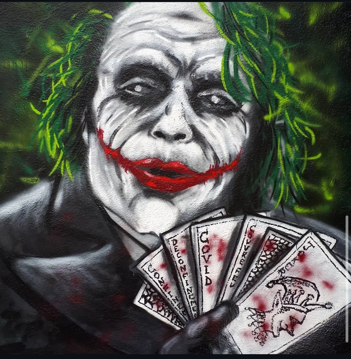 Graffiti représentant le personnage de Joker avec un visage maquillé en blanc, des lèvres rouges souriantes, entouré de feuilles vertes, tenant des billets de banque avec des inscriptions liées au COVID-19 et à la pandémie.