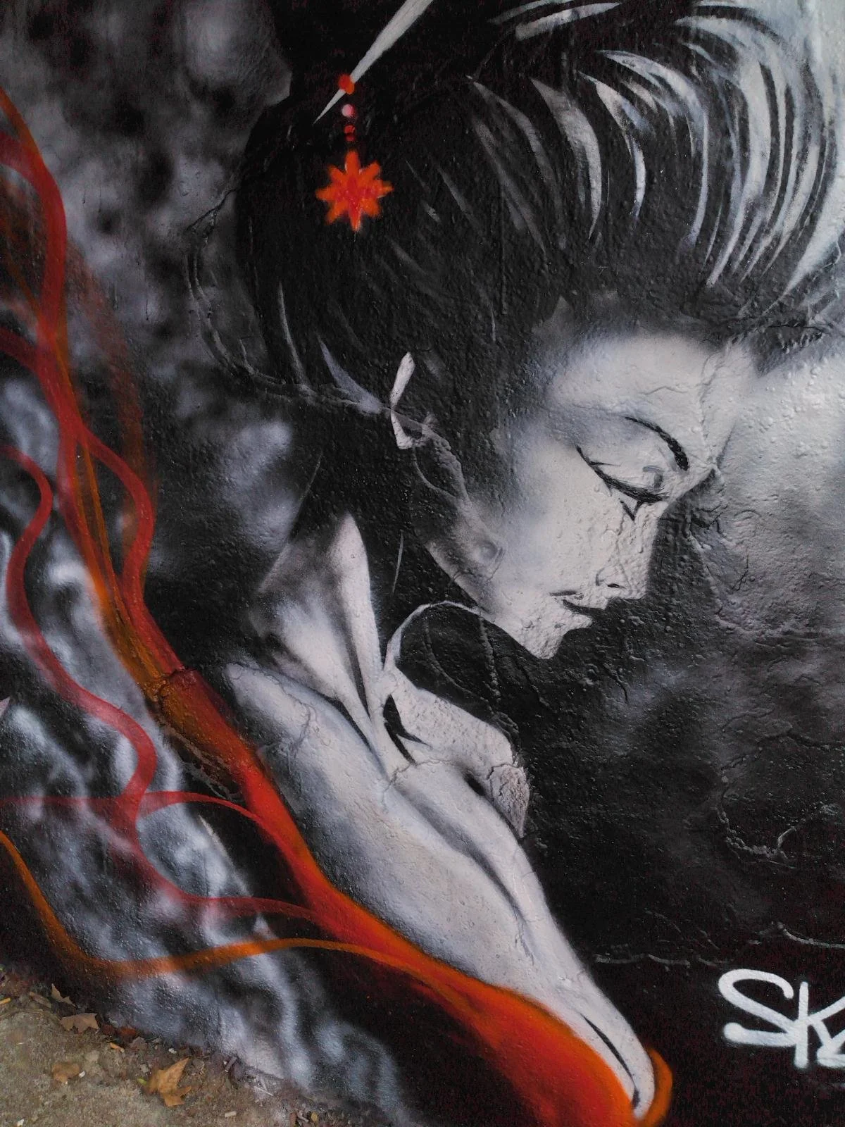 Un graffiti représentant une femme en noir et blanc, avec des détails de chevelure et visage expressifs, quelques éléments rouges et oranges sur le côté.