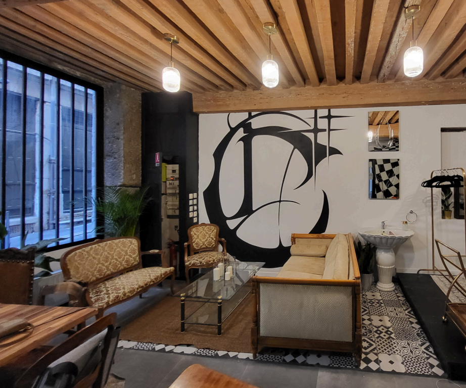 Salon intérieur avec mobilier vintage, mur avec peinture abstraite noire et blanche, suspension en verre, grande fenêtre avec grille métallique, décorations variées.