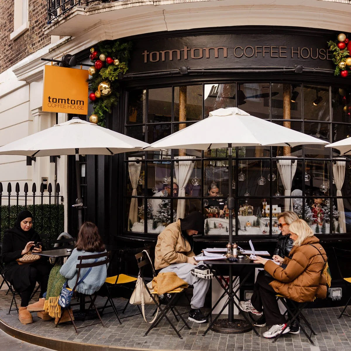 People sitting outside Tomtom Coffee House during the day, with white umbrellas and holiday decorations on the building.