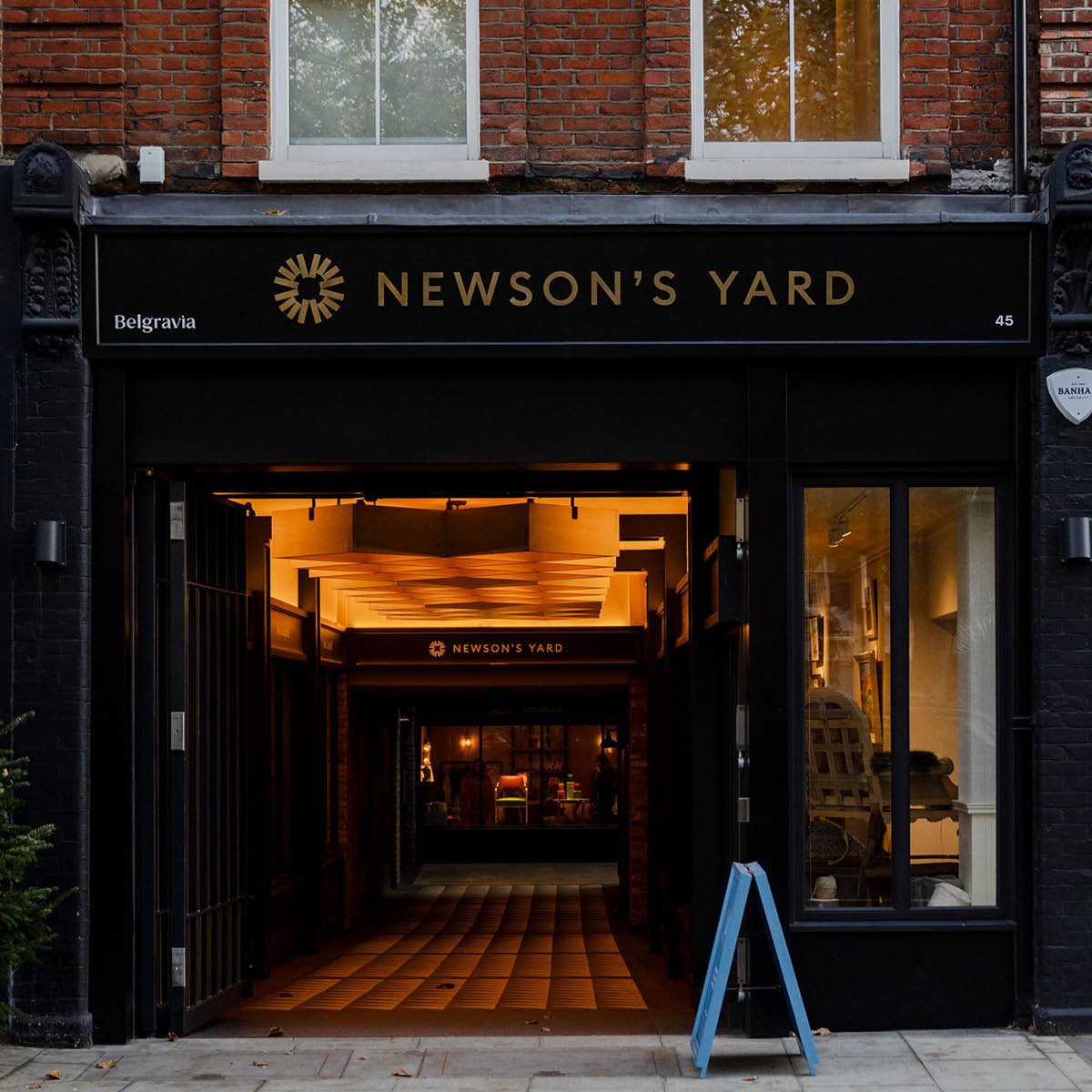 The storefront of Newson's Yard, a trendy shop or gallery with a black exterior, gold signage, and an illuminated interior visible through the open entrance, located at 45 Belgravia.