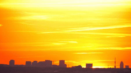 Sunset over a city skyline with orange and yellow sky and dark buildings.