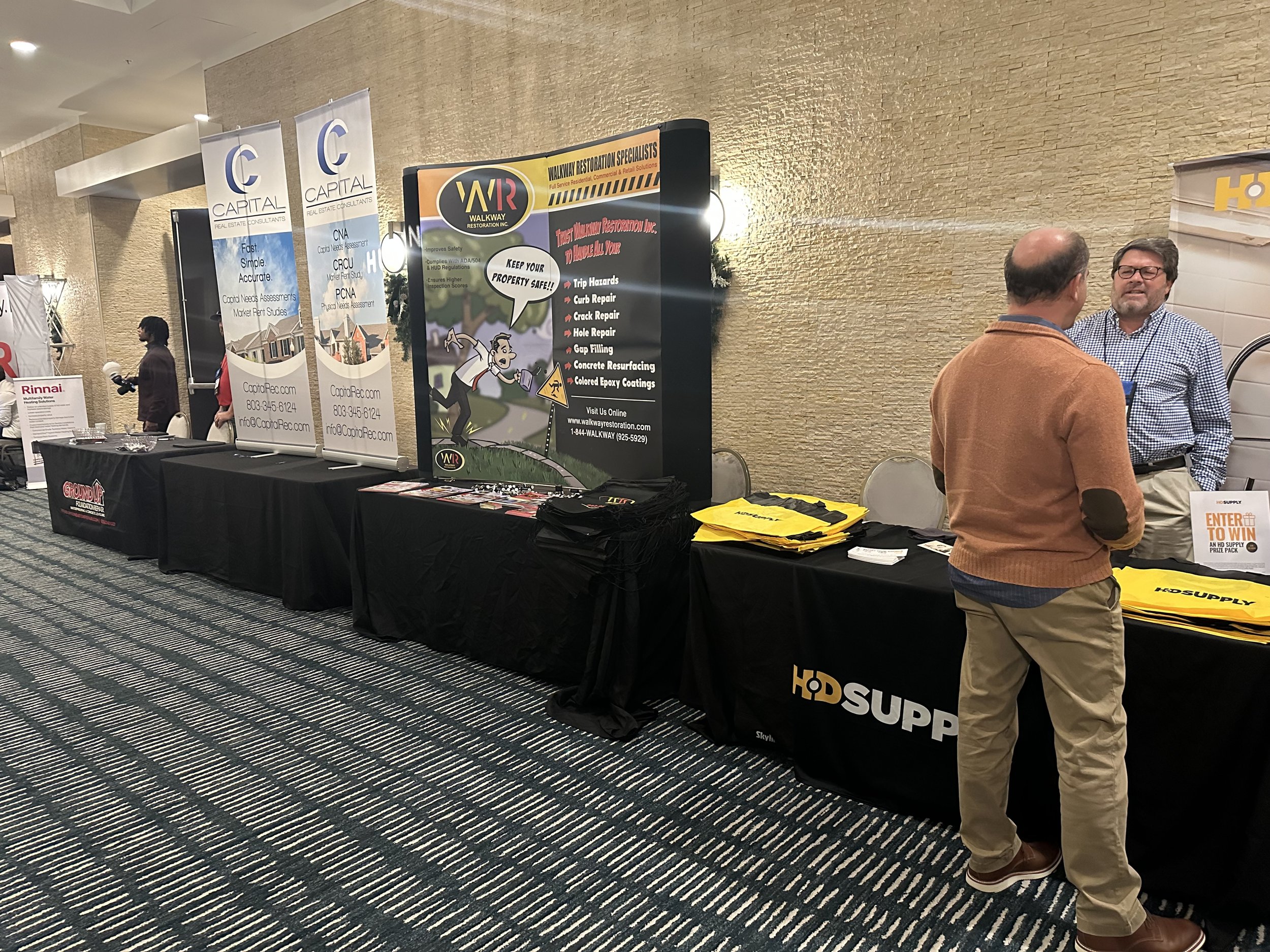Trade show with marketing booths, banners, and two men talking at an HD Supply table.