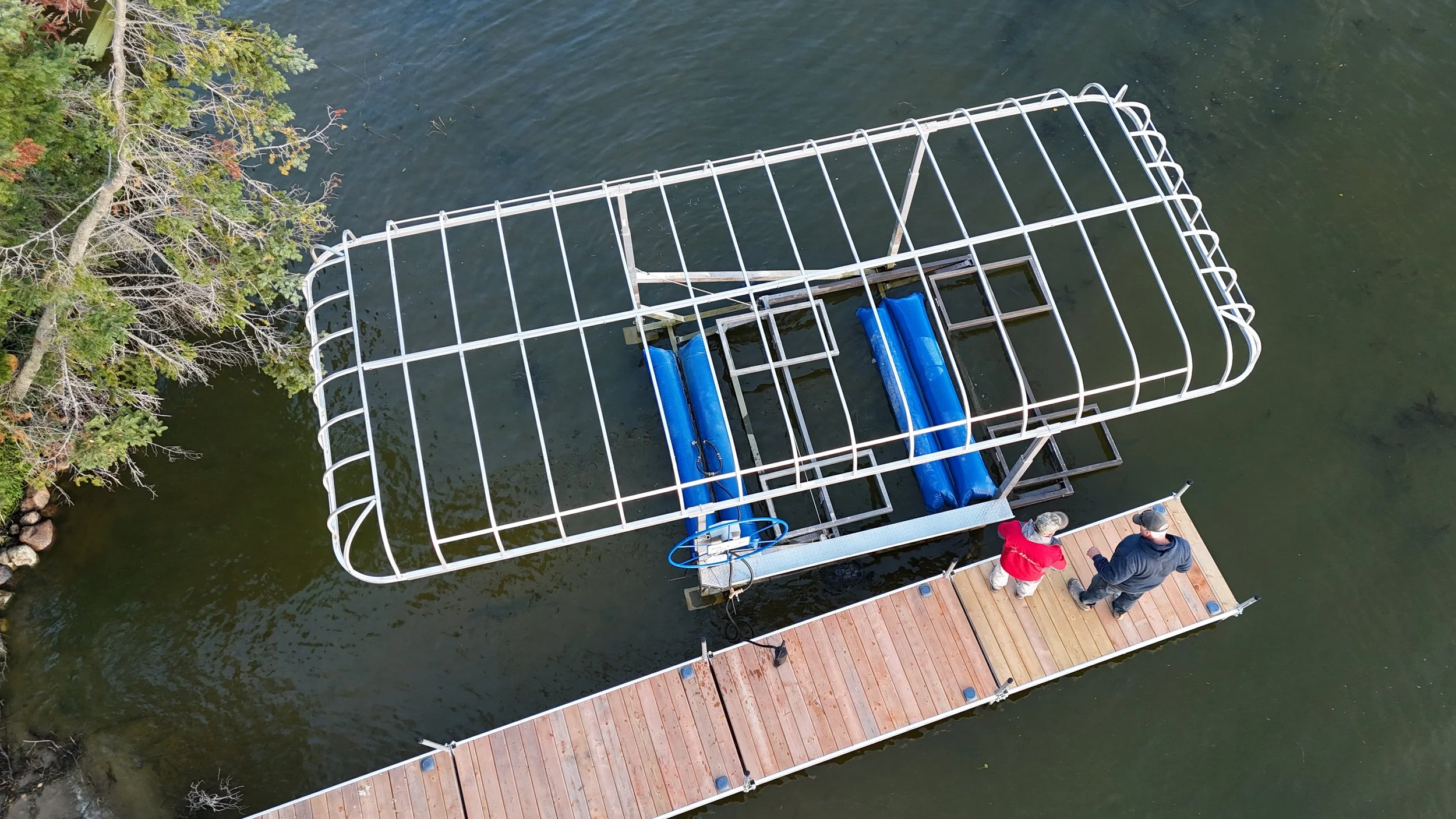 Aerial view of a boat dock with a metal canopy being floated into position