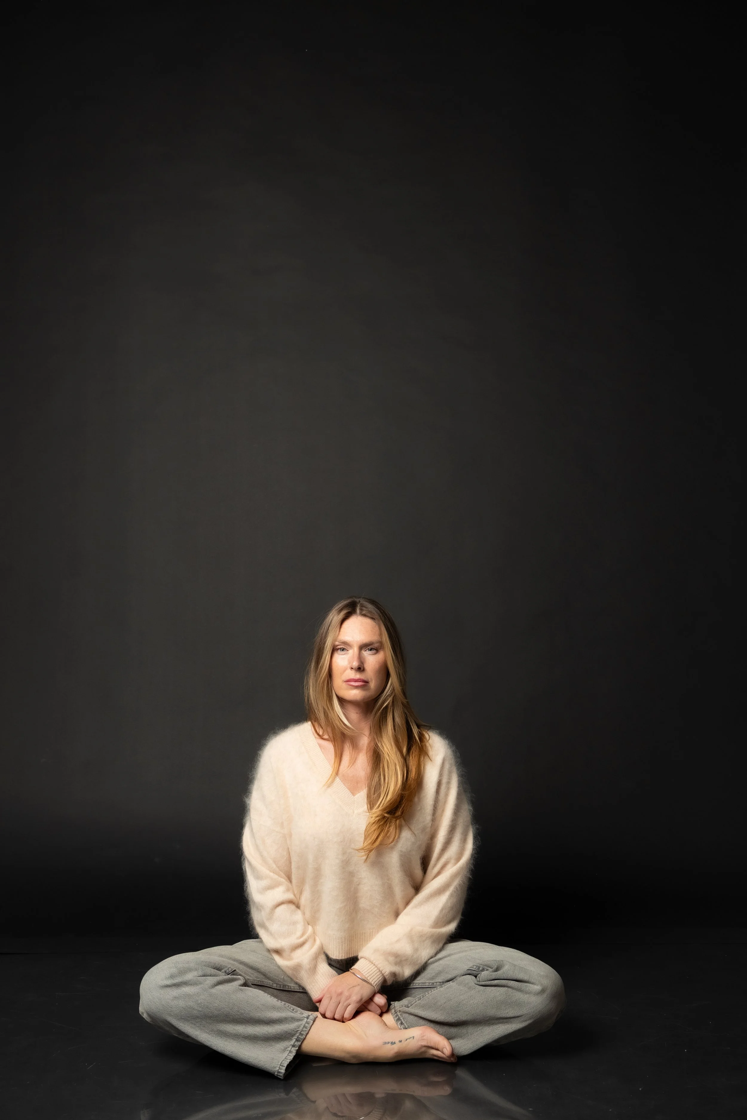 Ashlee Jowett - Contact me. Woman with long hair sitting cross-legged on a reflective surface against a dark background.