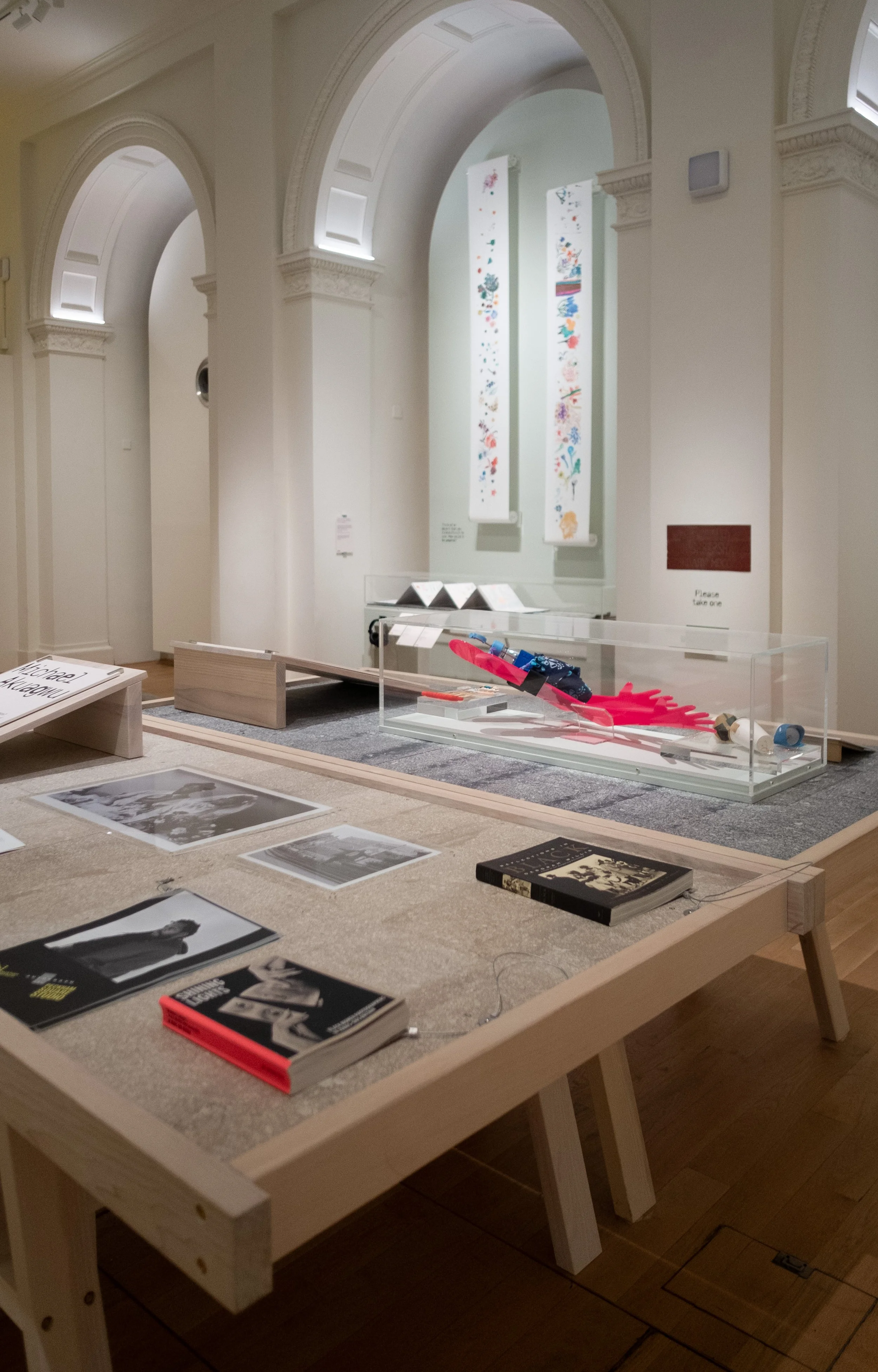 Display table with books and photographs in a museum with white walls and arched architectural details.