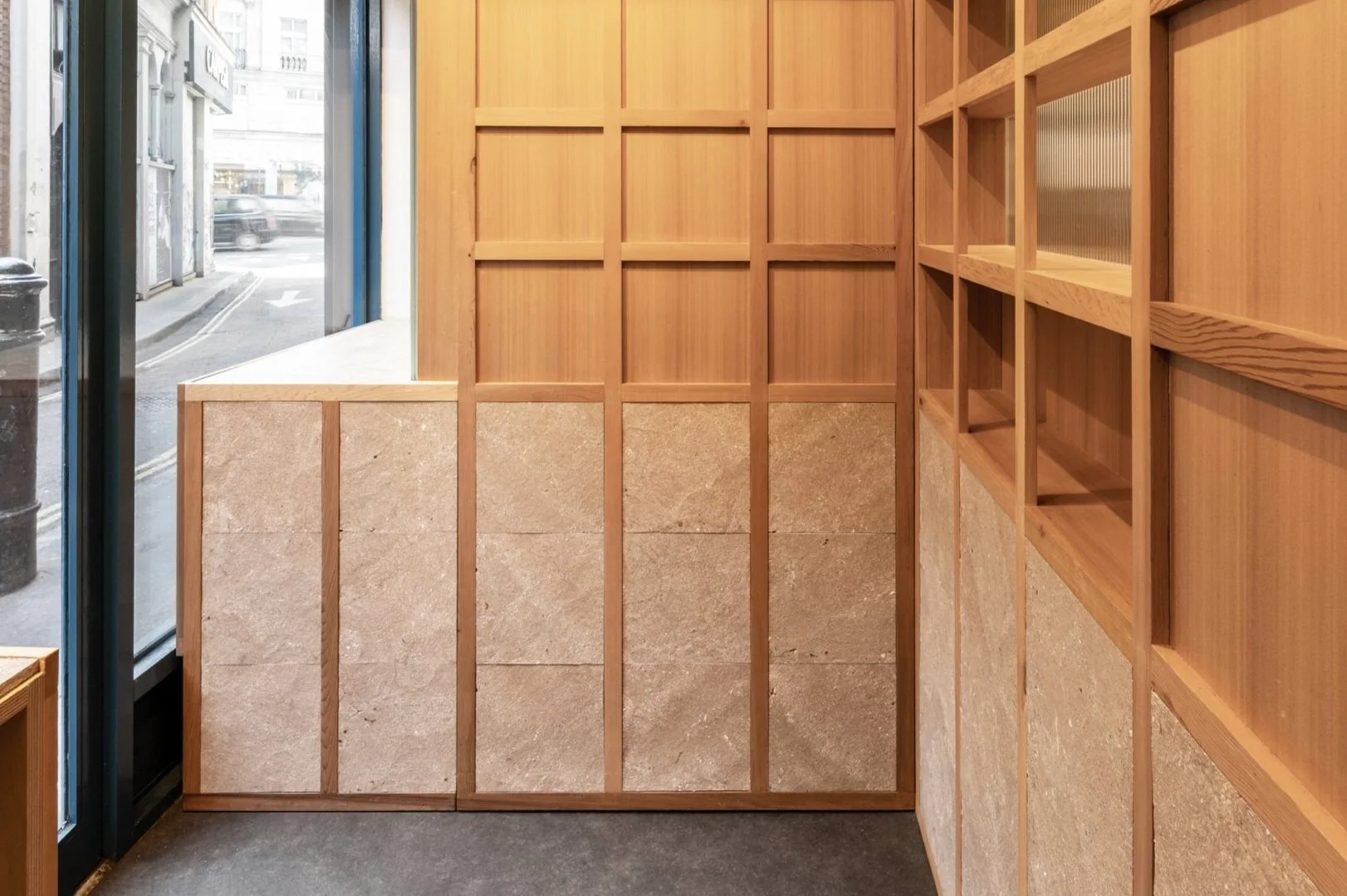 Interior of a store or cafe with wooden shelves and a window showing the street outside.