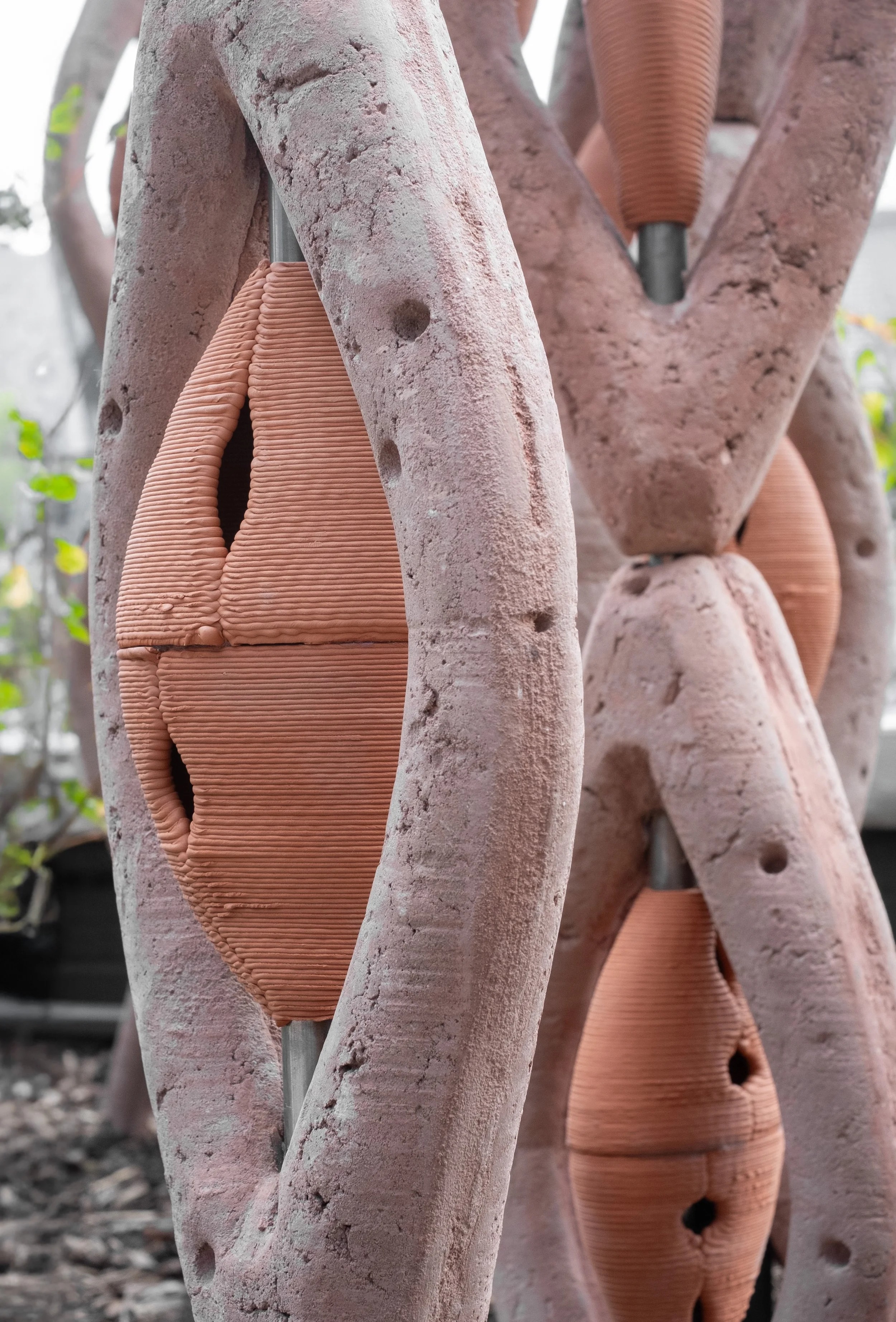 Close-up of a textured wooden sculpture with abstract shapes, featuring smooth, rounded clay or ceramic elements in a reddish color integrated into the sculpture.