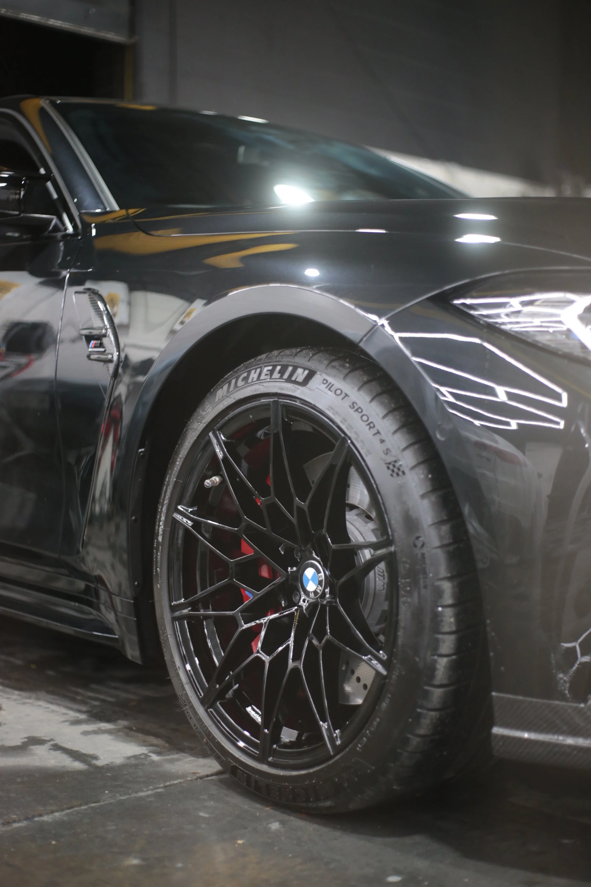A black BMW car with a sleek, sporty design, featuring a close-up view of the front wheel and part of the vehicle's side in a dimly lit garage or showroom.