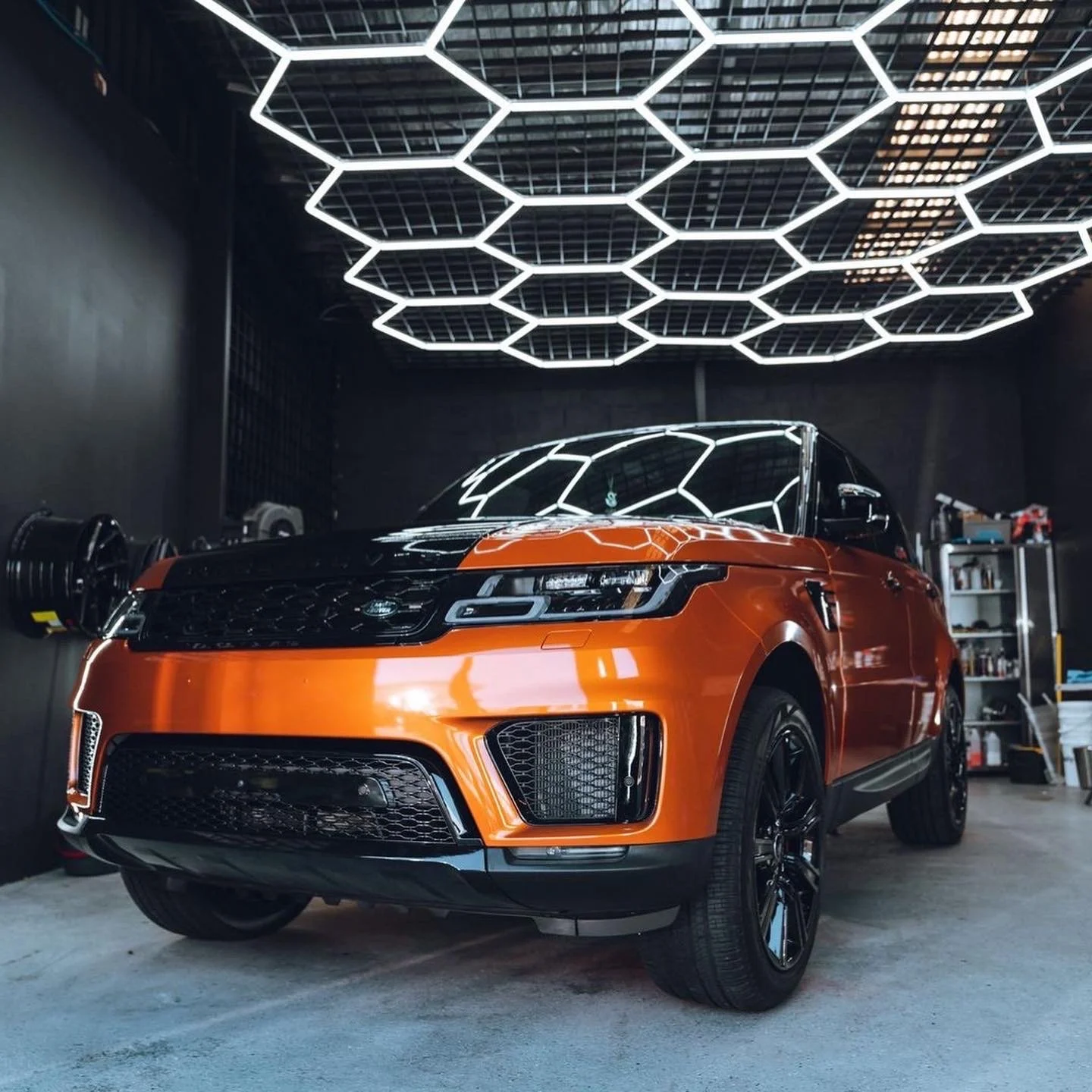 An orange and black luxury SUV parked in a garage with a modern hexagon-shaped ceiling light fixture.