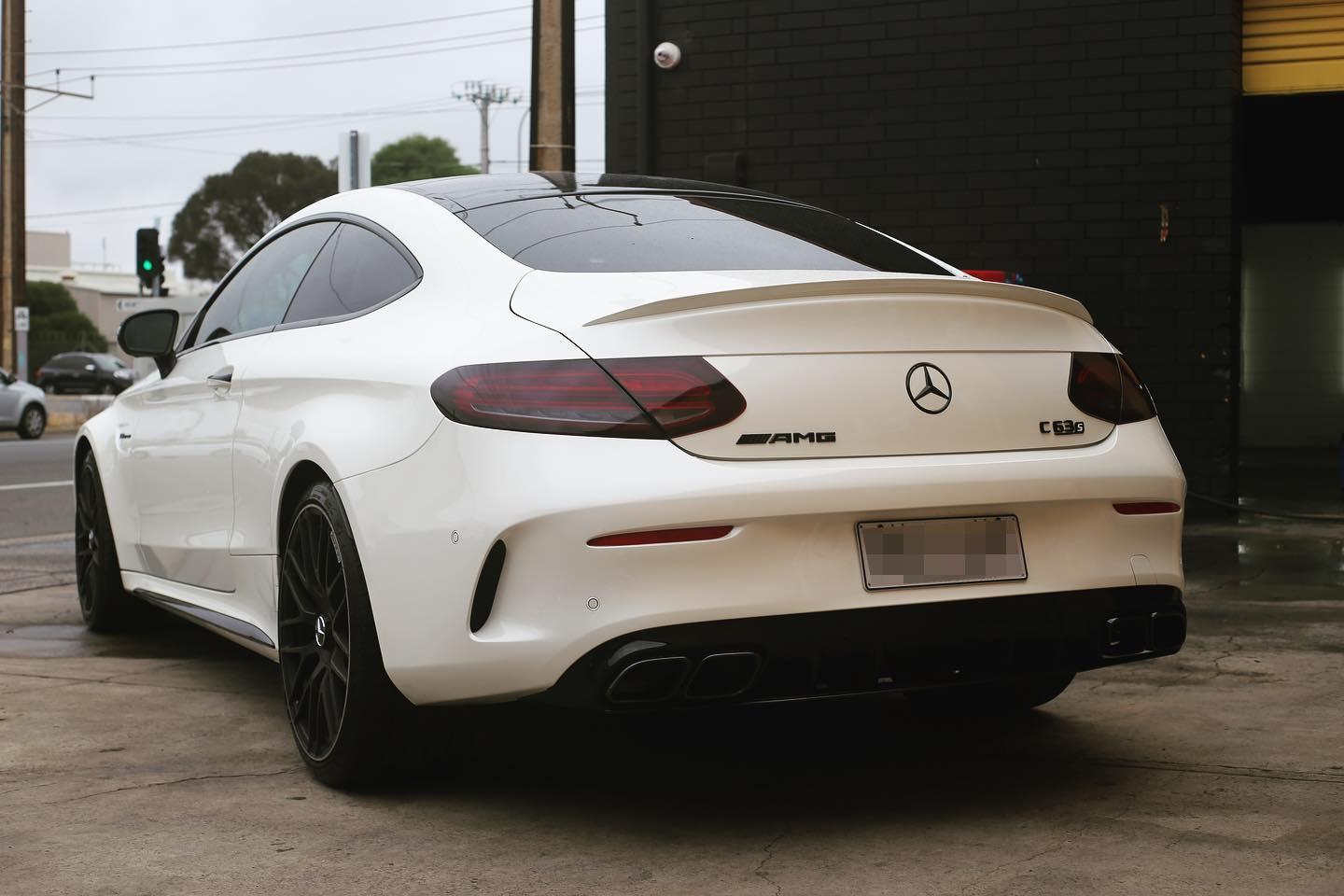 A white Mercedes-Benz C63S AMG coupe parked outdoors, showing the rear view with black wheels, Mercedes-Benz emblem, AMG badge, and dual exhaust pipes.