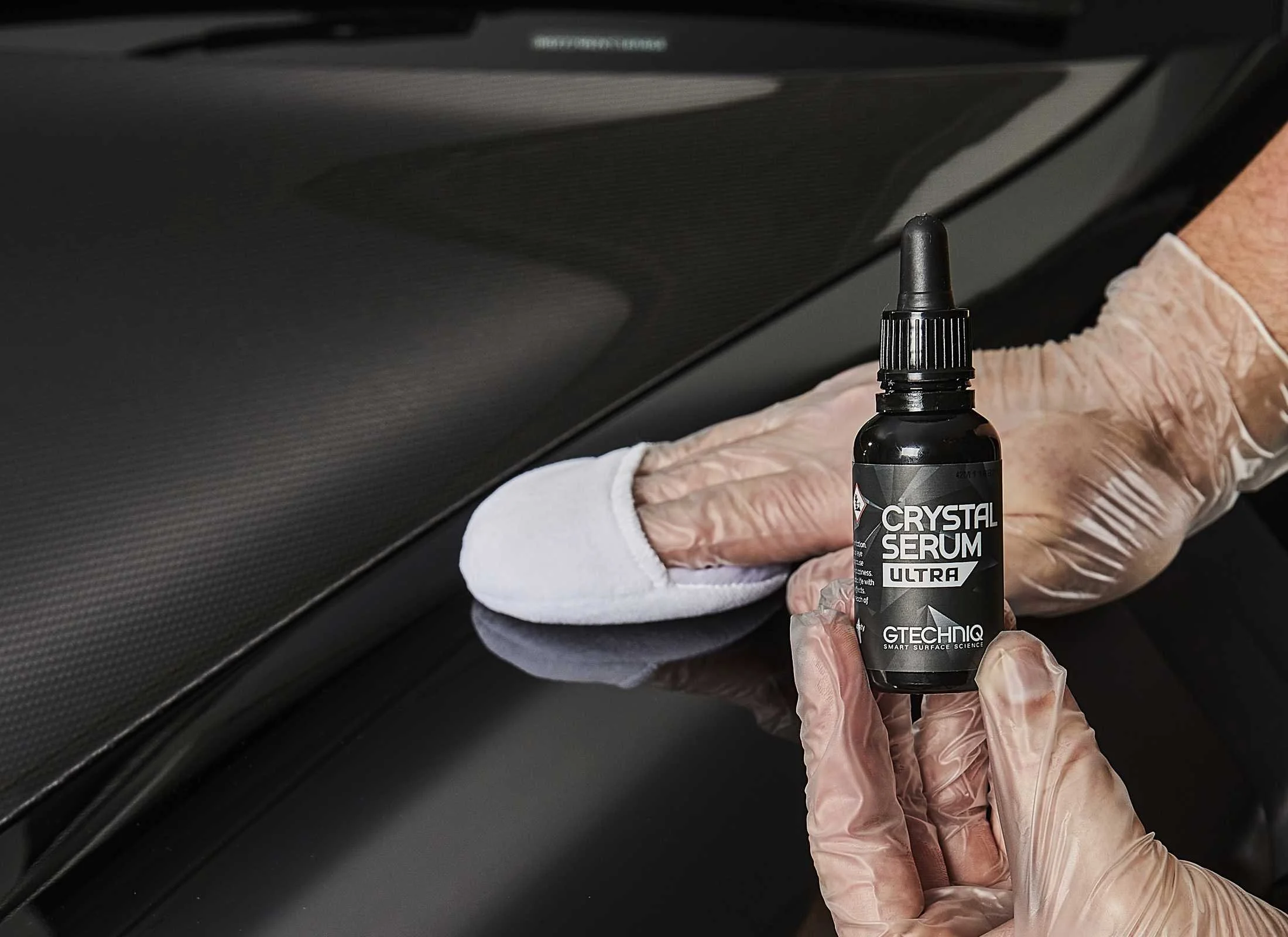 A person wearing gloves applying a dark surface coating using a small bottle of Crystal Serum Ultra by Gtechniq.