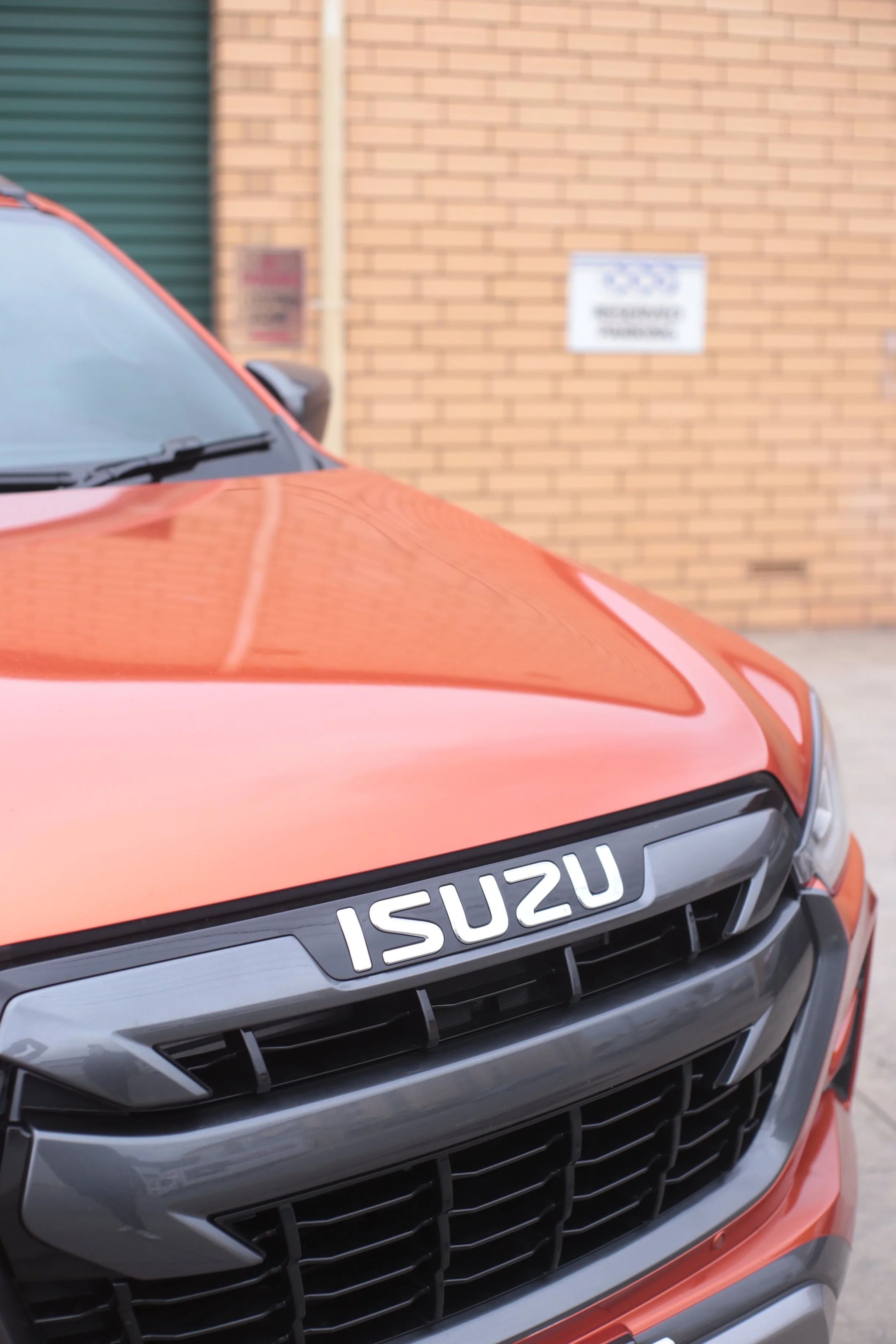 Close-up of the front of an orange Isuzu vehicle parked outside, showing the grille and hood with the Isuzu logo.