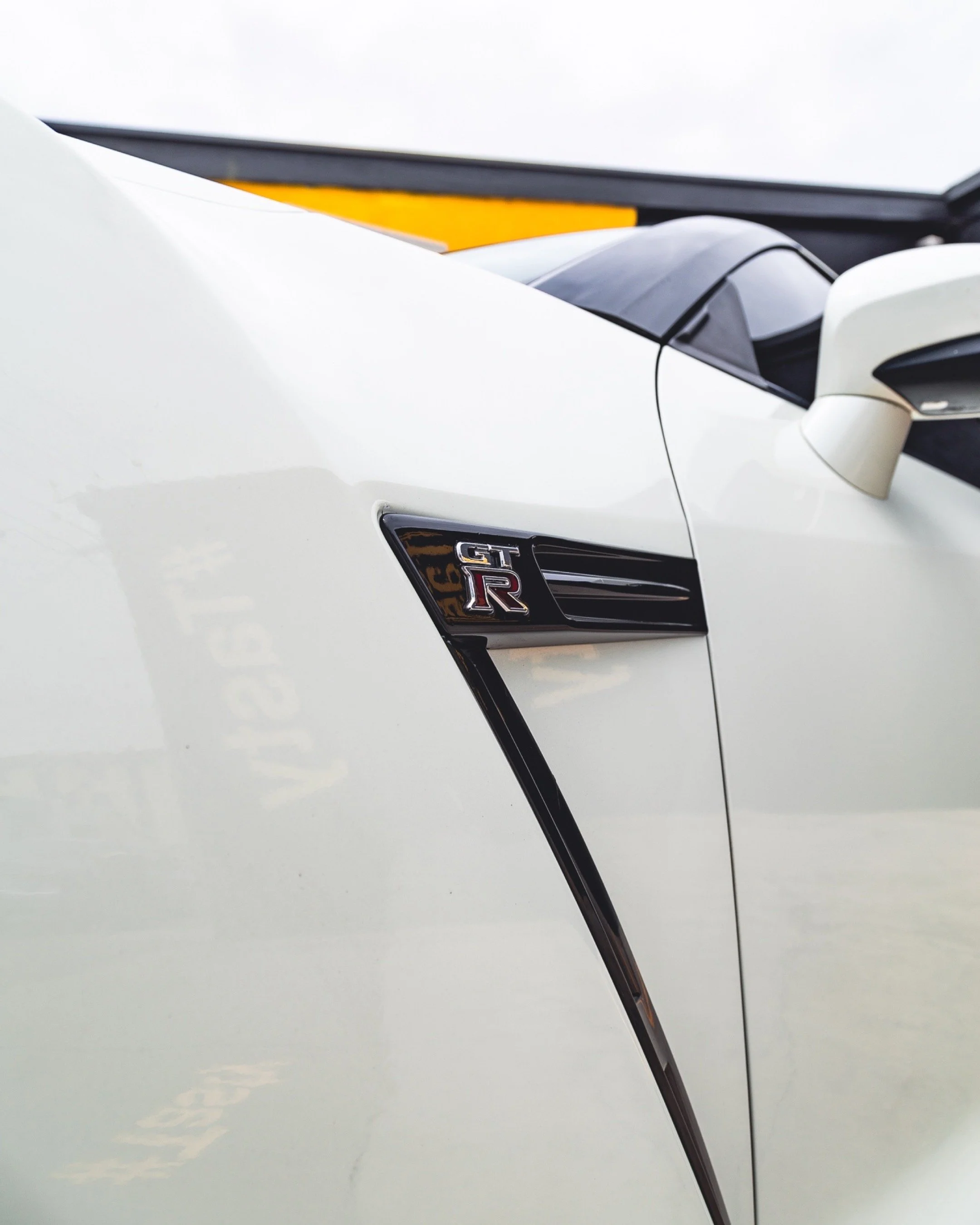 Close-up of a white Nissan GT-R car, focusing on the front right side, with the GT-R badge visible.