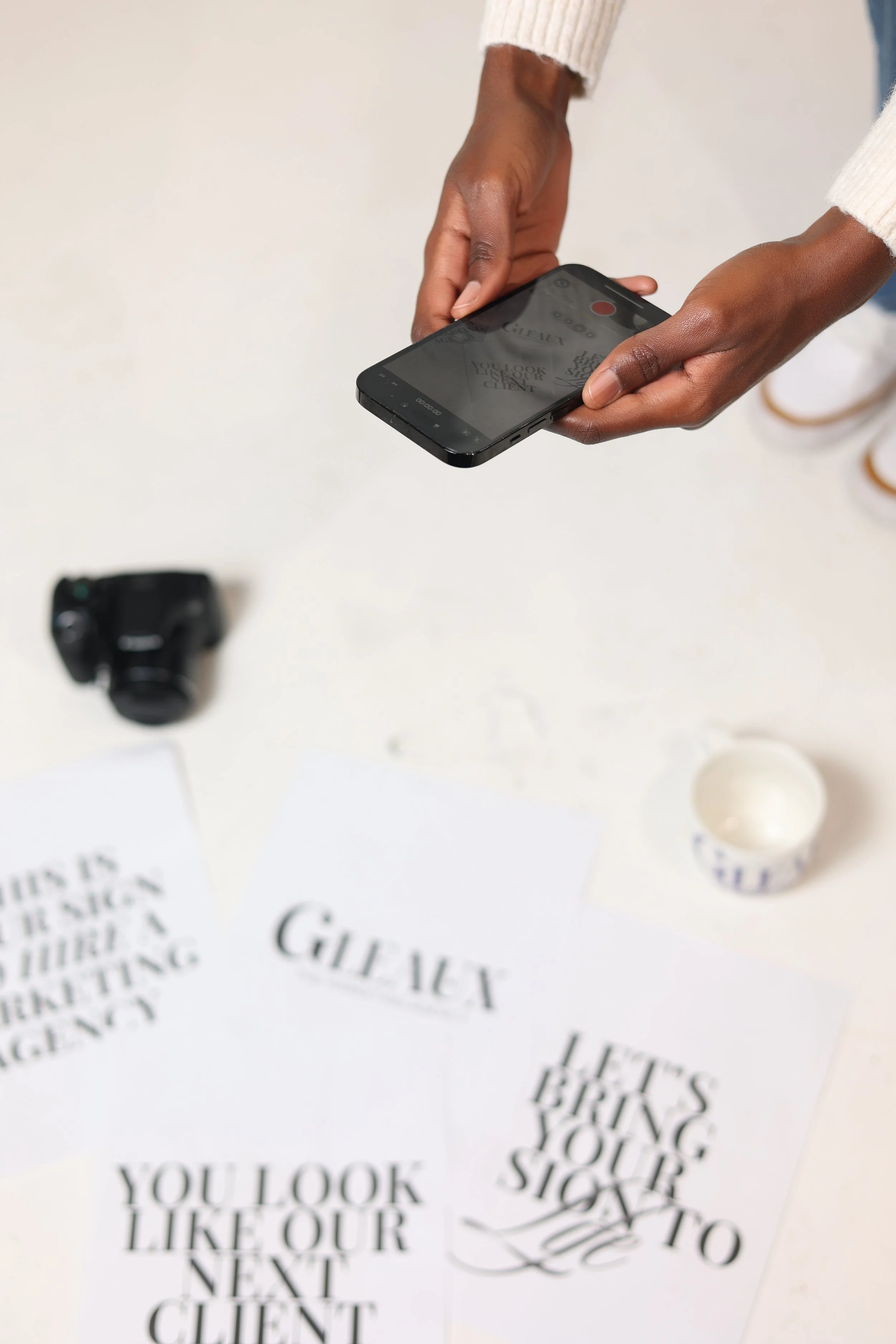a set of hands taking a picture of papers on the ground