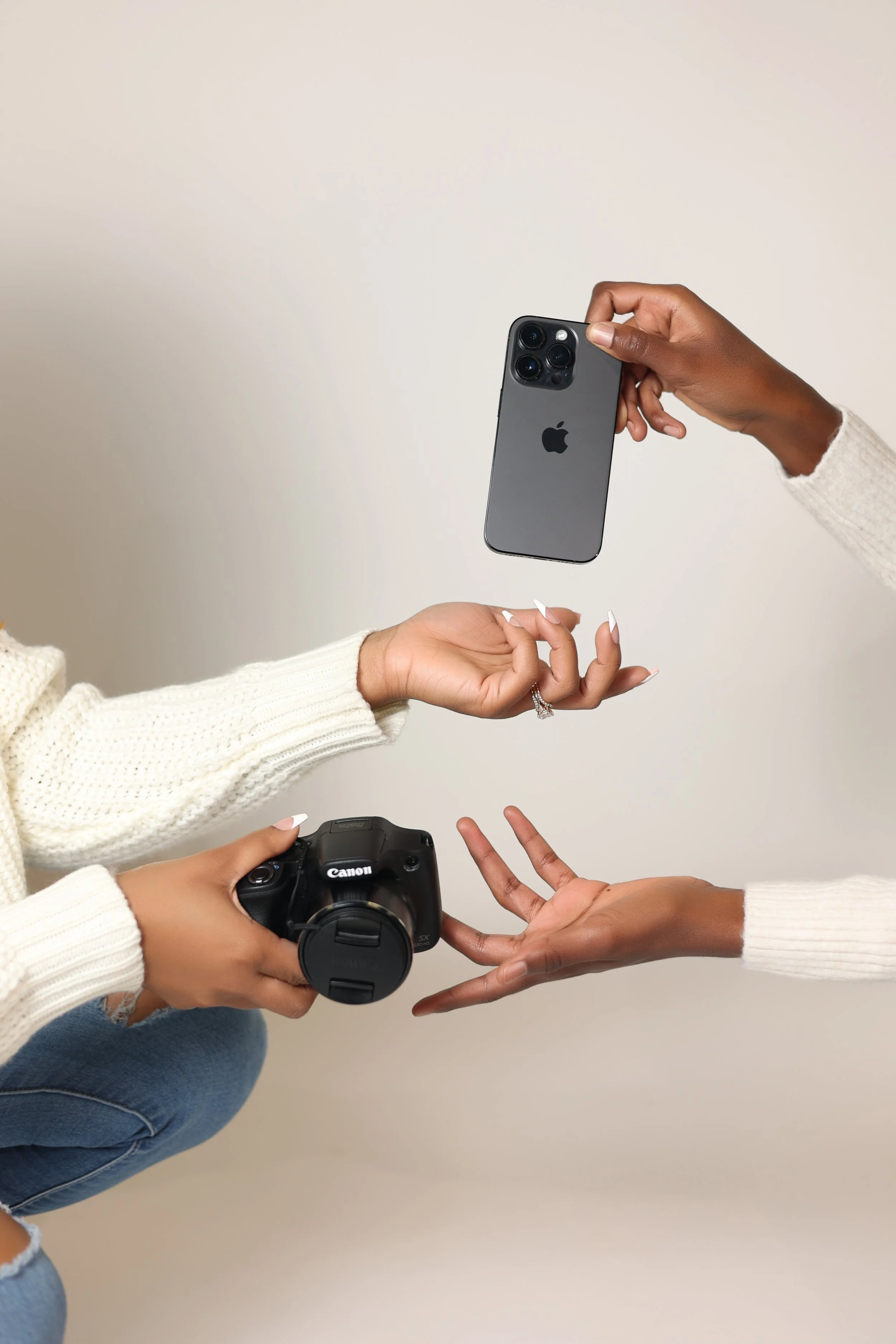 2 sets of hands giving each other a cannon camera and a iphone