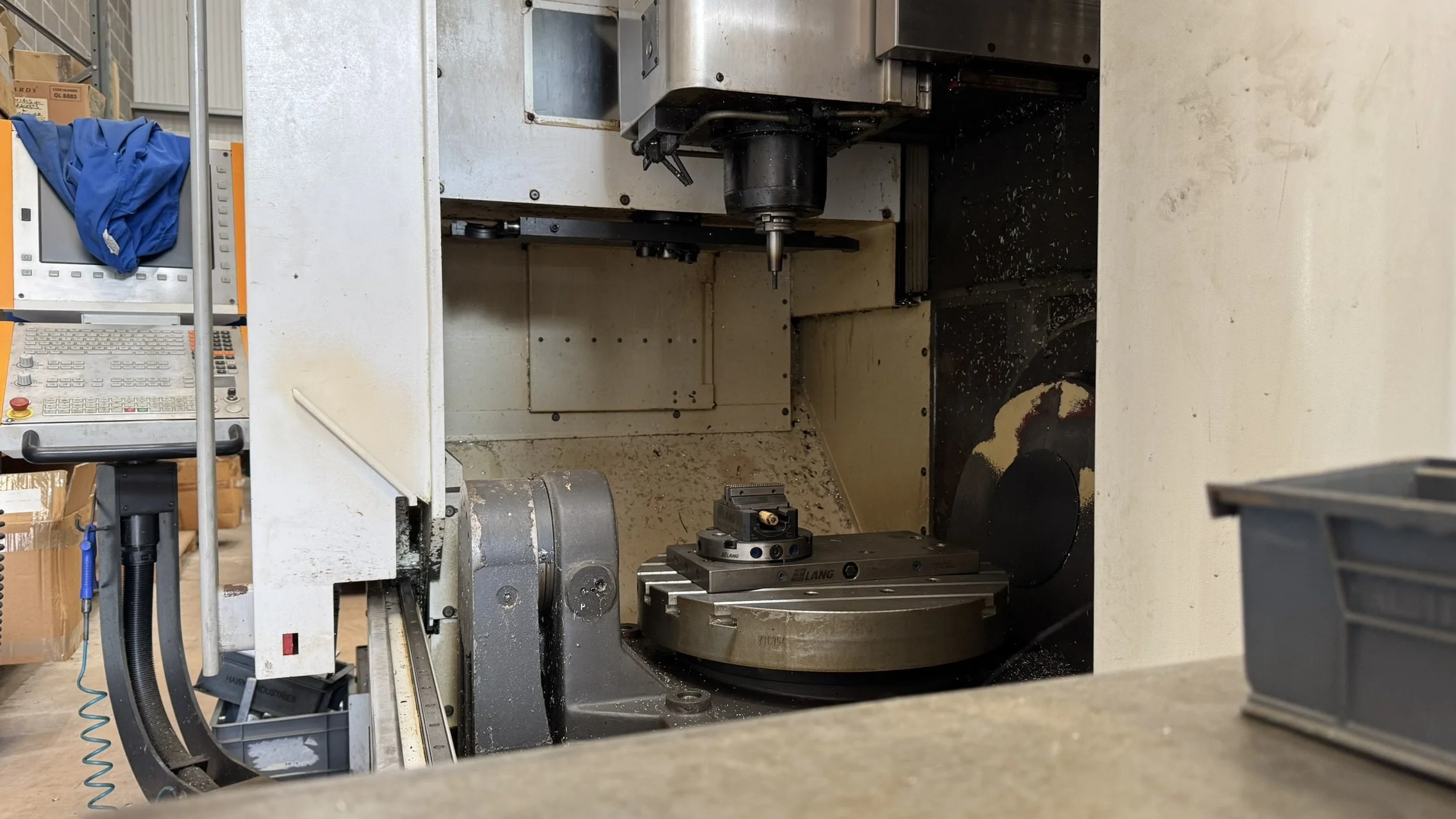 View of a CNC machine in an industrial workshop, with metal shavings inside and a control panel on the side.