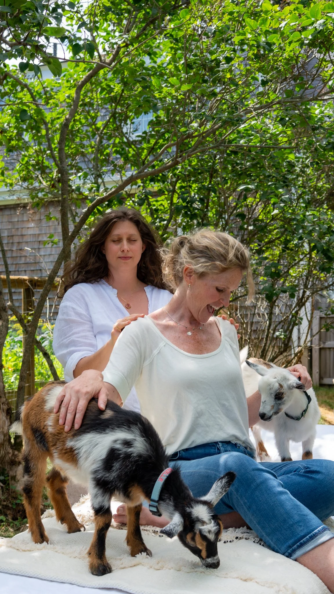 A female client receiving energy healing from Corbin Chase while sitting on a bed outside, holding a small goat.