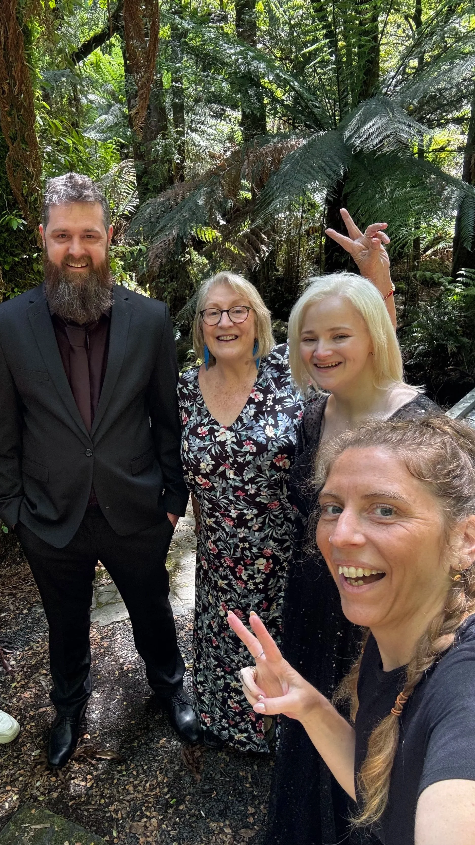 A group of five people, four women and one man, smiling and posing for a selfie in a lush, green forest.