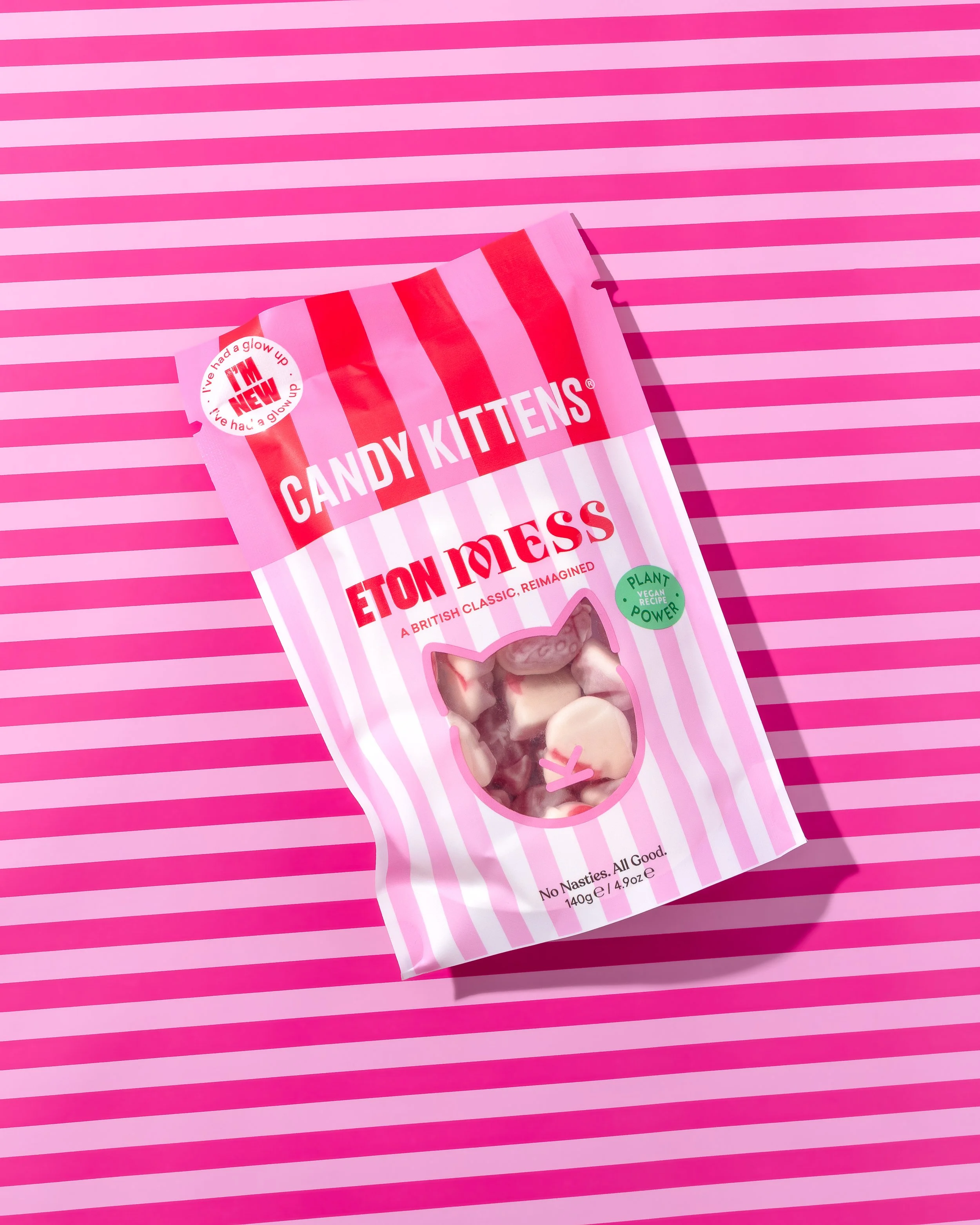 Pink and white striped candy packaging with a see-through window showing white and pink candies, placed on a pink striped background.