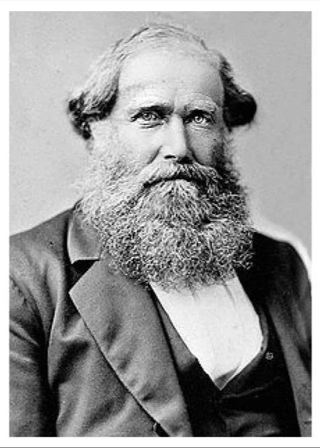 Black and white portrait of a man with a full beard, mustache, and a serious expression, wearing a suit and waistcoat.