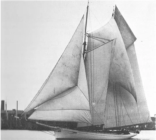 A black and white photograph of a large sailing ship with multiple sails unfurled, docked at a harbor.
