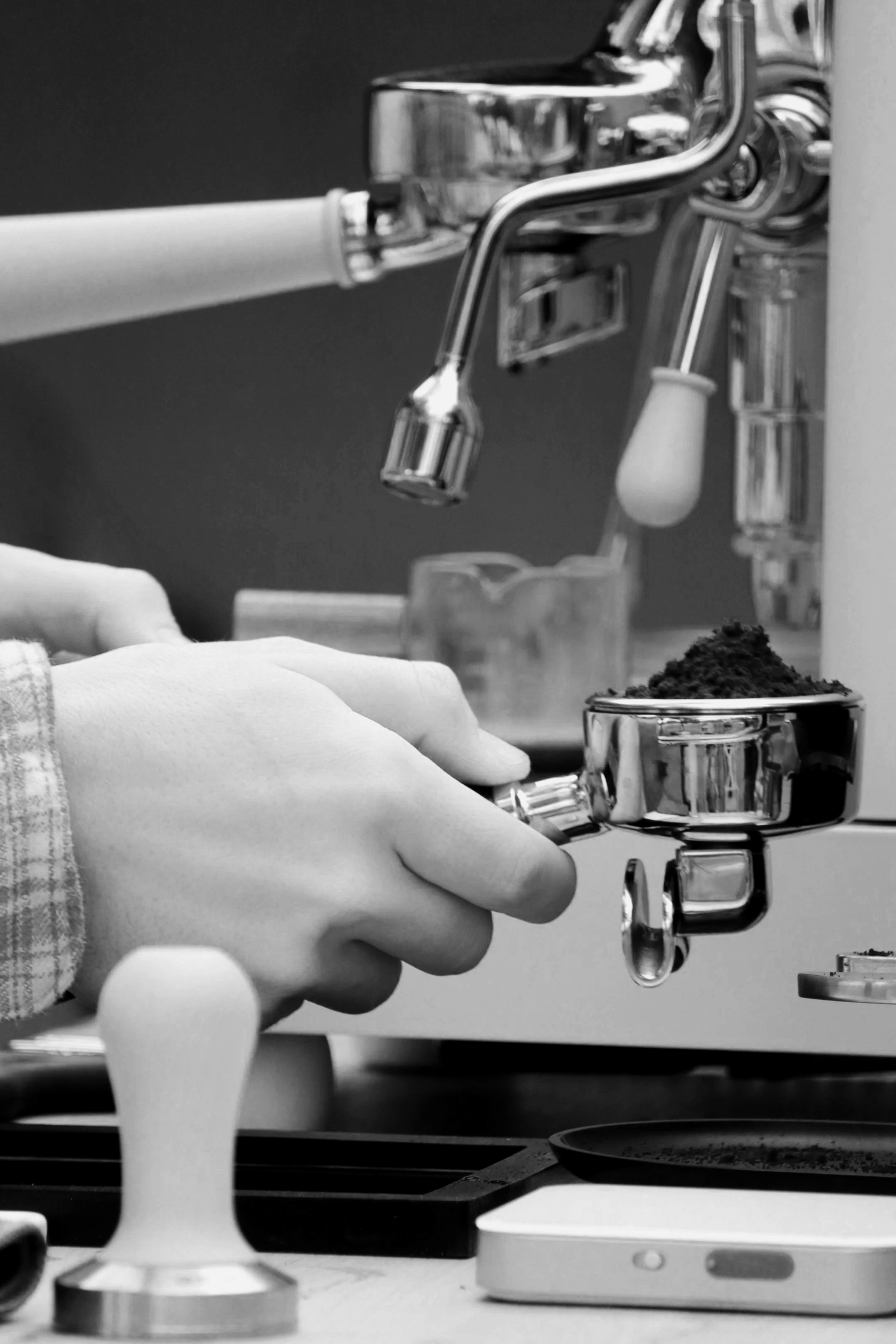Hands holding a tool under a professional espresso machine.