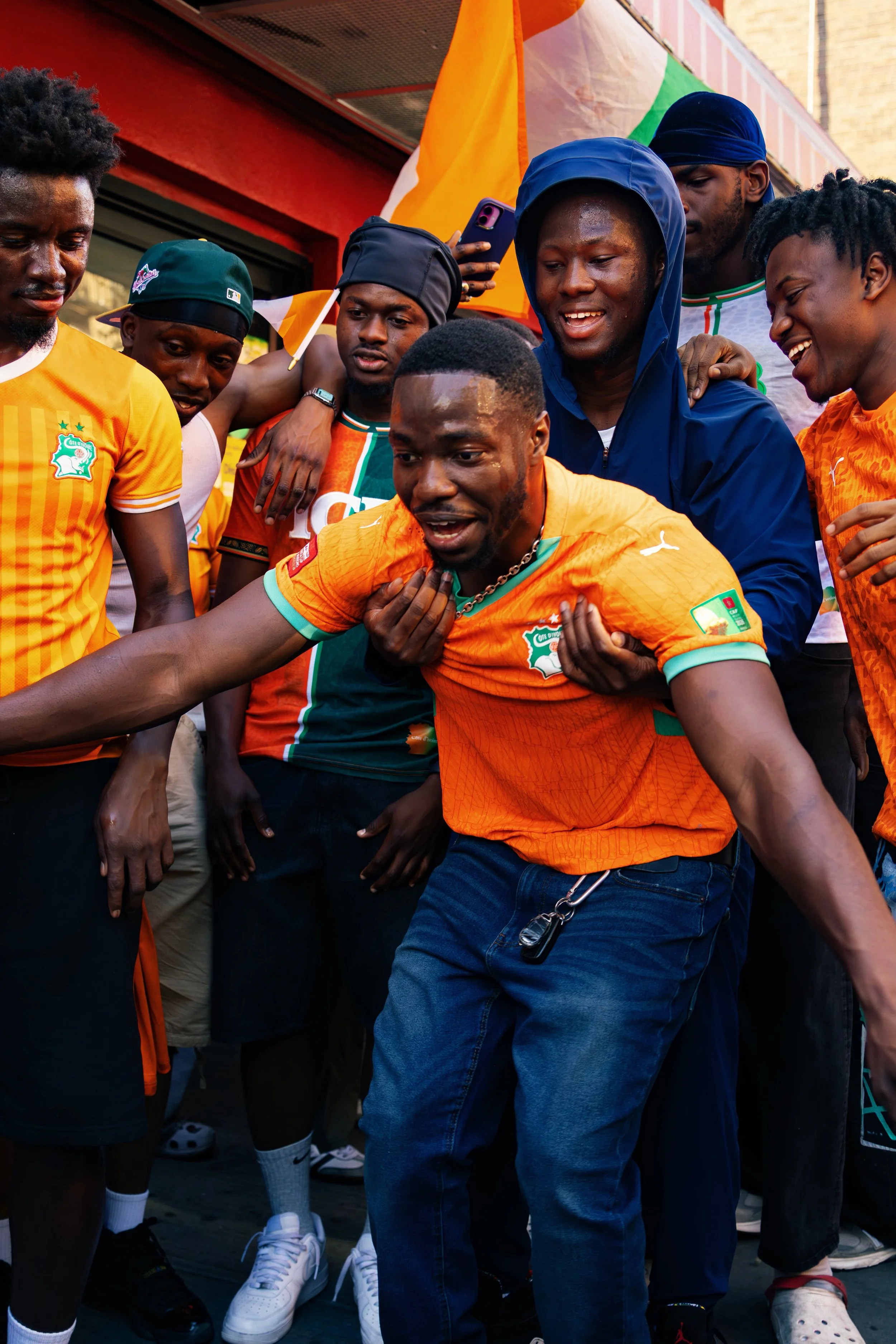 Group of young men celebrating and having fun at an outdoor event with colorful flags in the background.