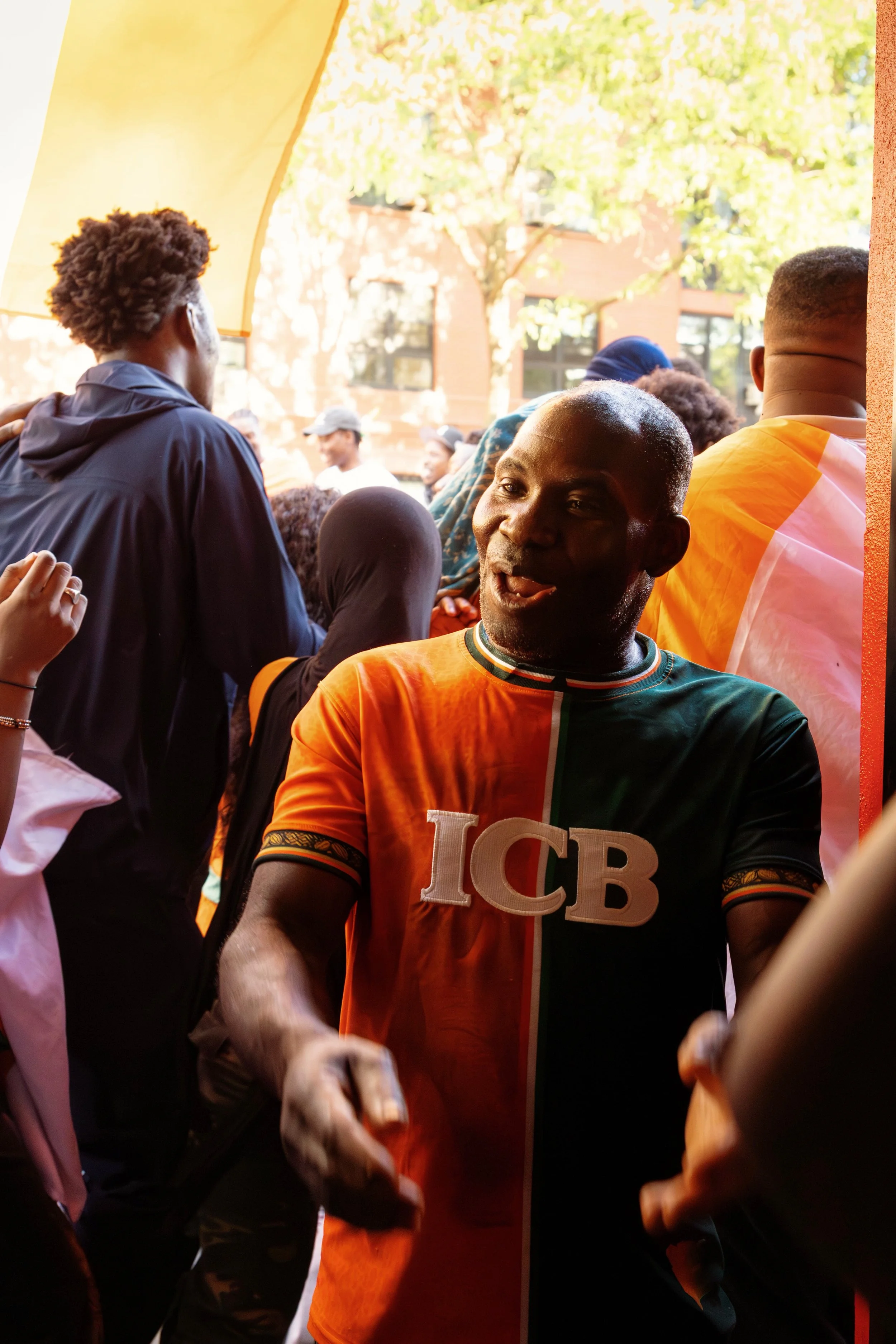 A group of people at an outdoor event, with one person prominently in the foreground wearing a colorful sports jersey with 'FCB' on it, smiling and interacting with others.