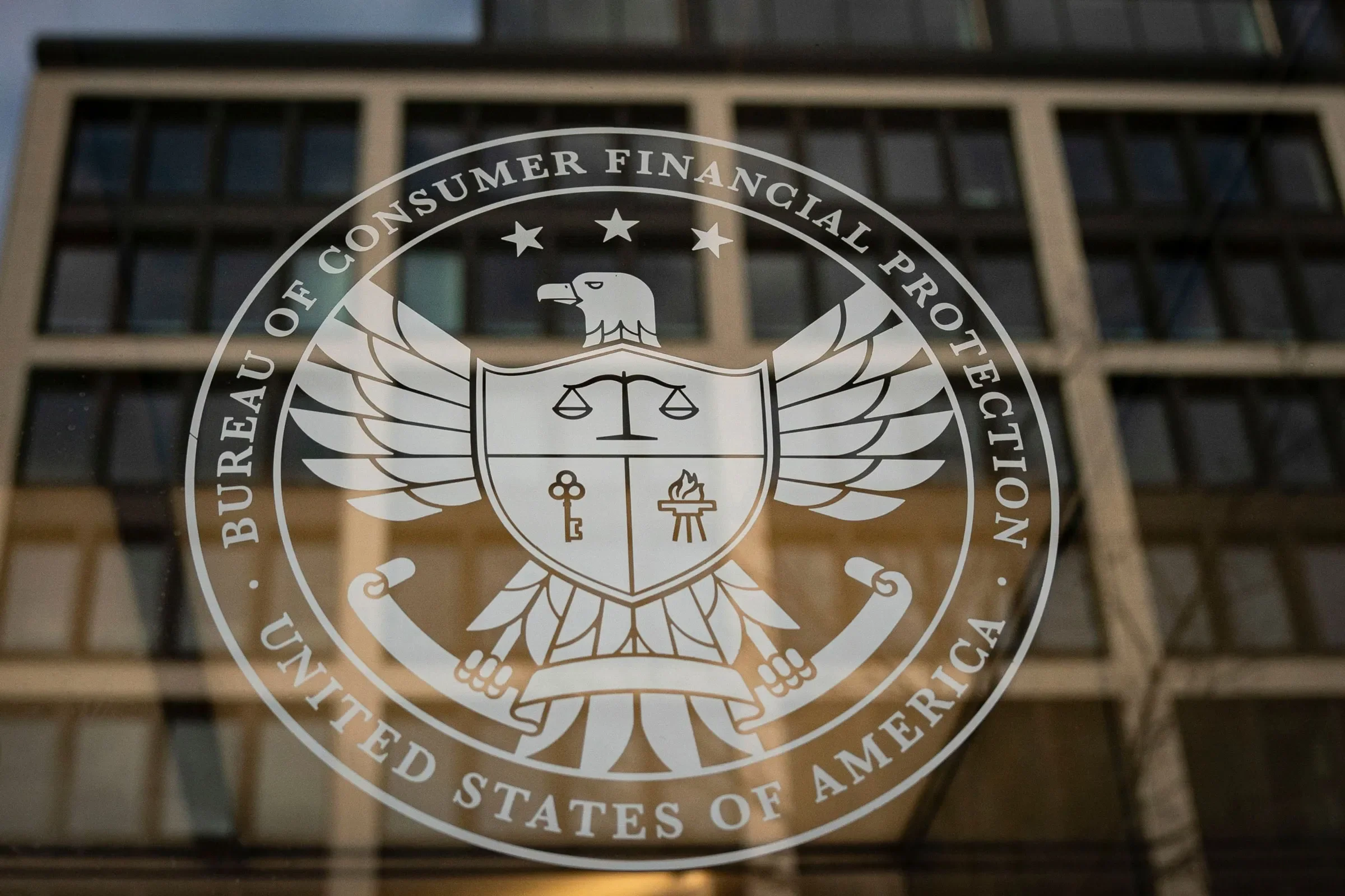 Pane of glass with an etched logo of the Consumer Financial Protection Bureau with the words "Bureau of Consumer Financial Protection United States of America" with an eagle in the center, a shield in front of it's chest.
