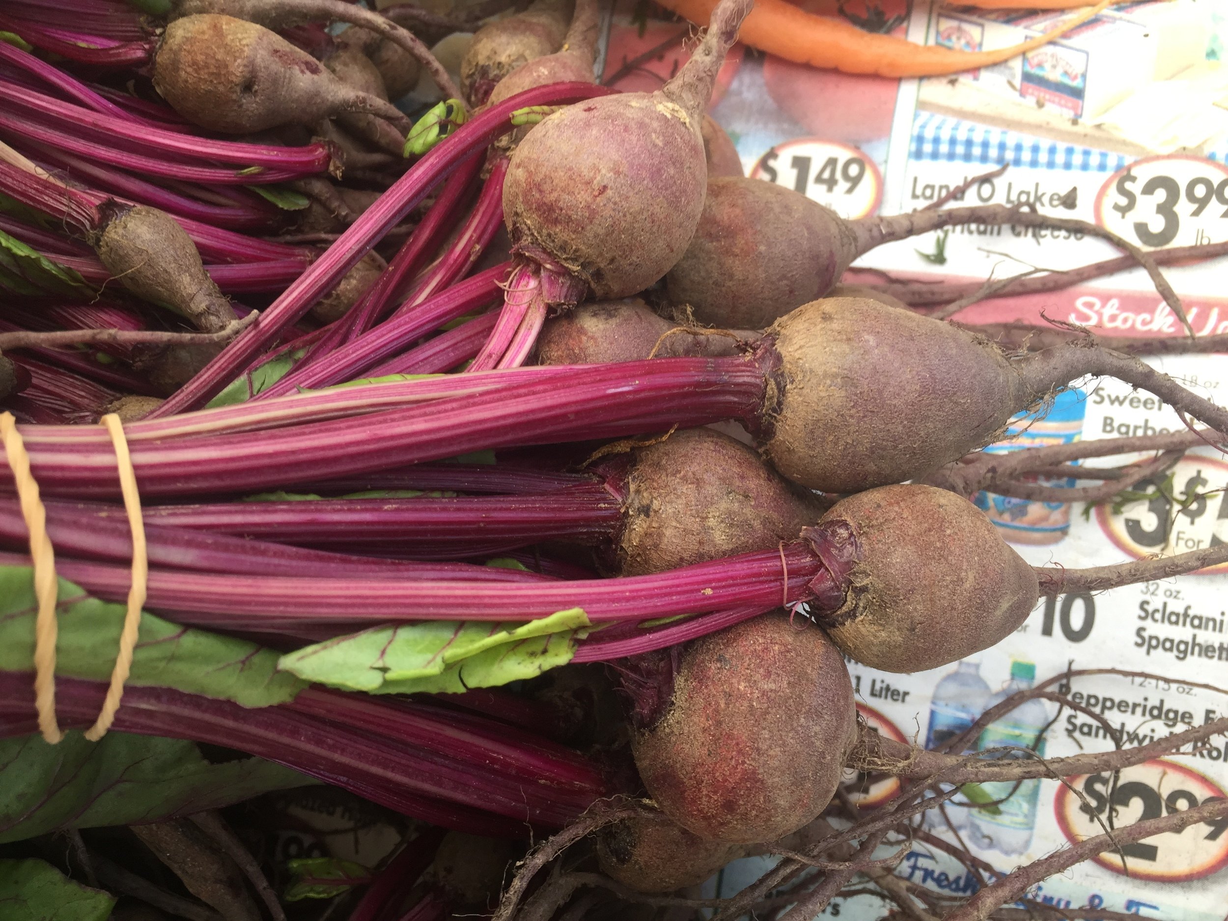 A close-up of fresh beets with their red stalks and green leaves, displayed in a market.