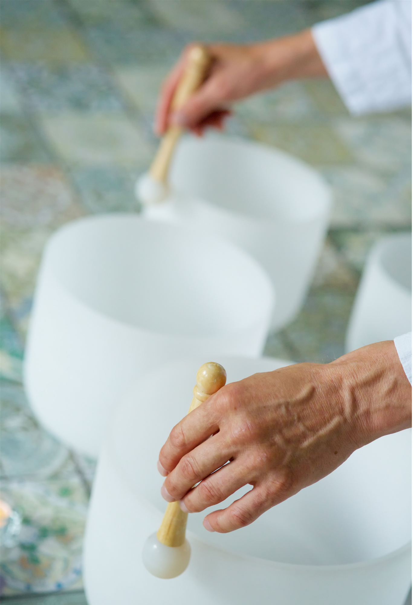 Close-up of a person's hand holding a wooden stick with a white spherical object, with blurred white objects behind.