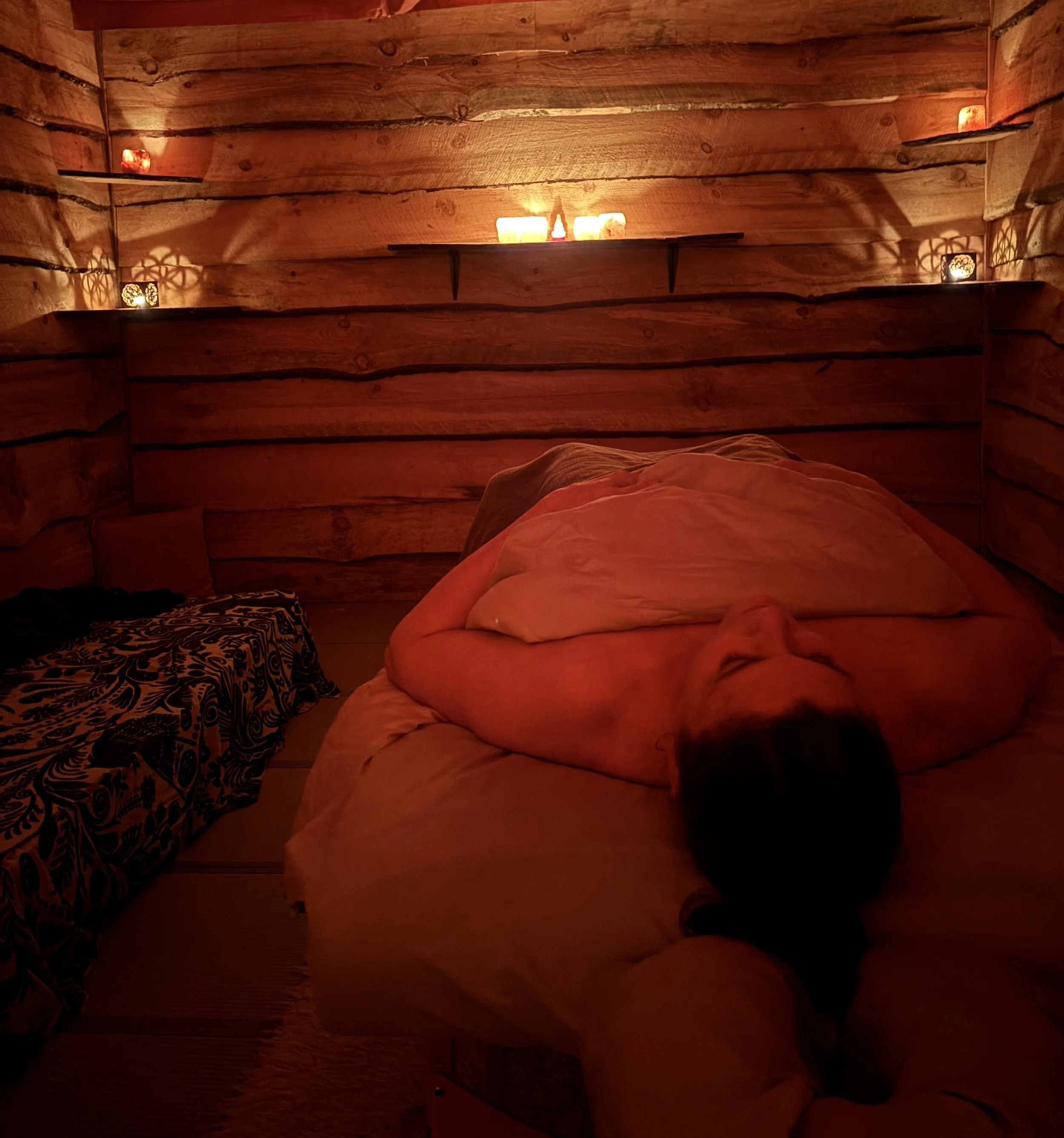 A cozy bedroom with wooden walls illuminated by candlelight and decorative lanterns, creating a warm and peaceful ambiance.