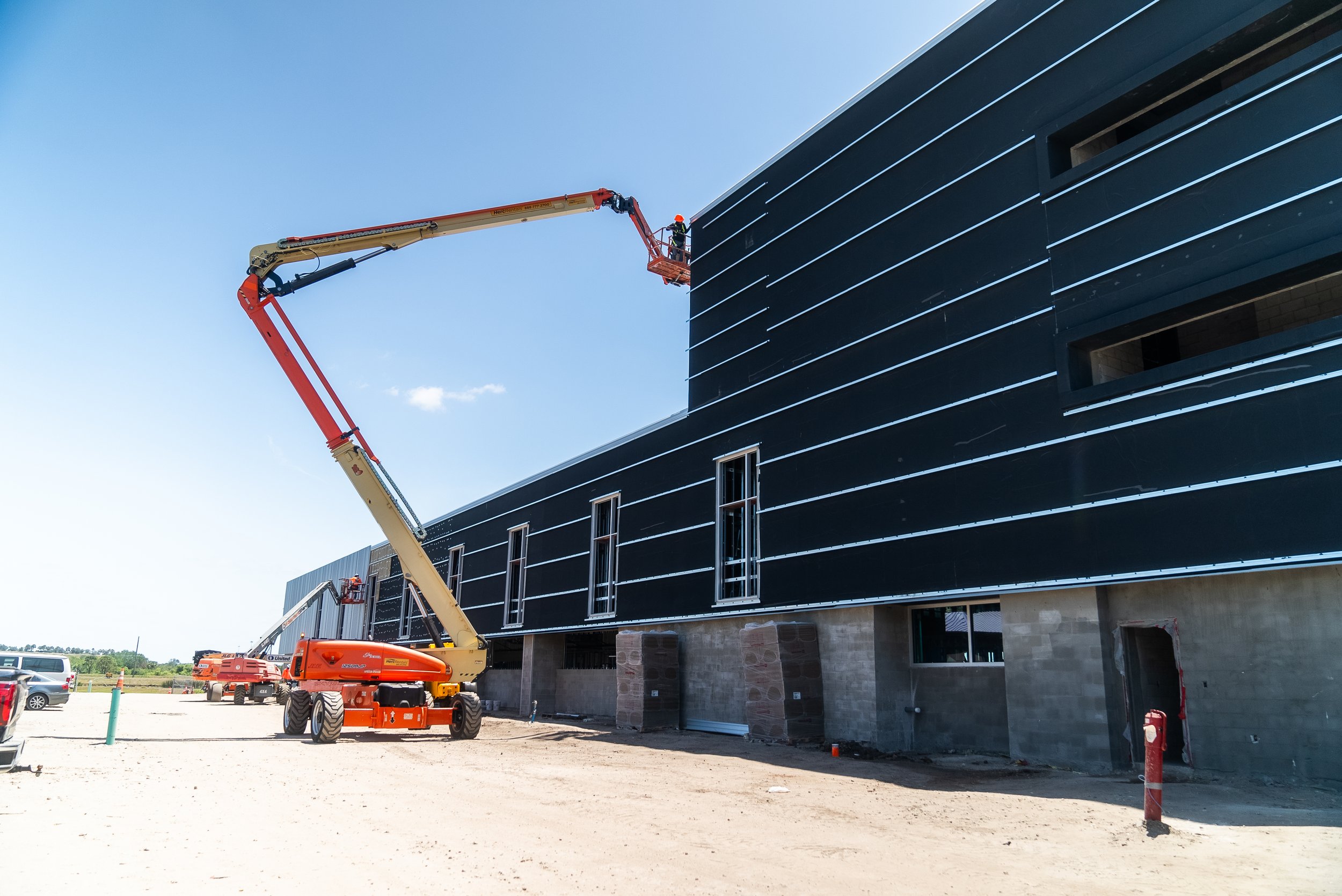 Construction site with a worker on a cherry picker lift against a building exterior.
