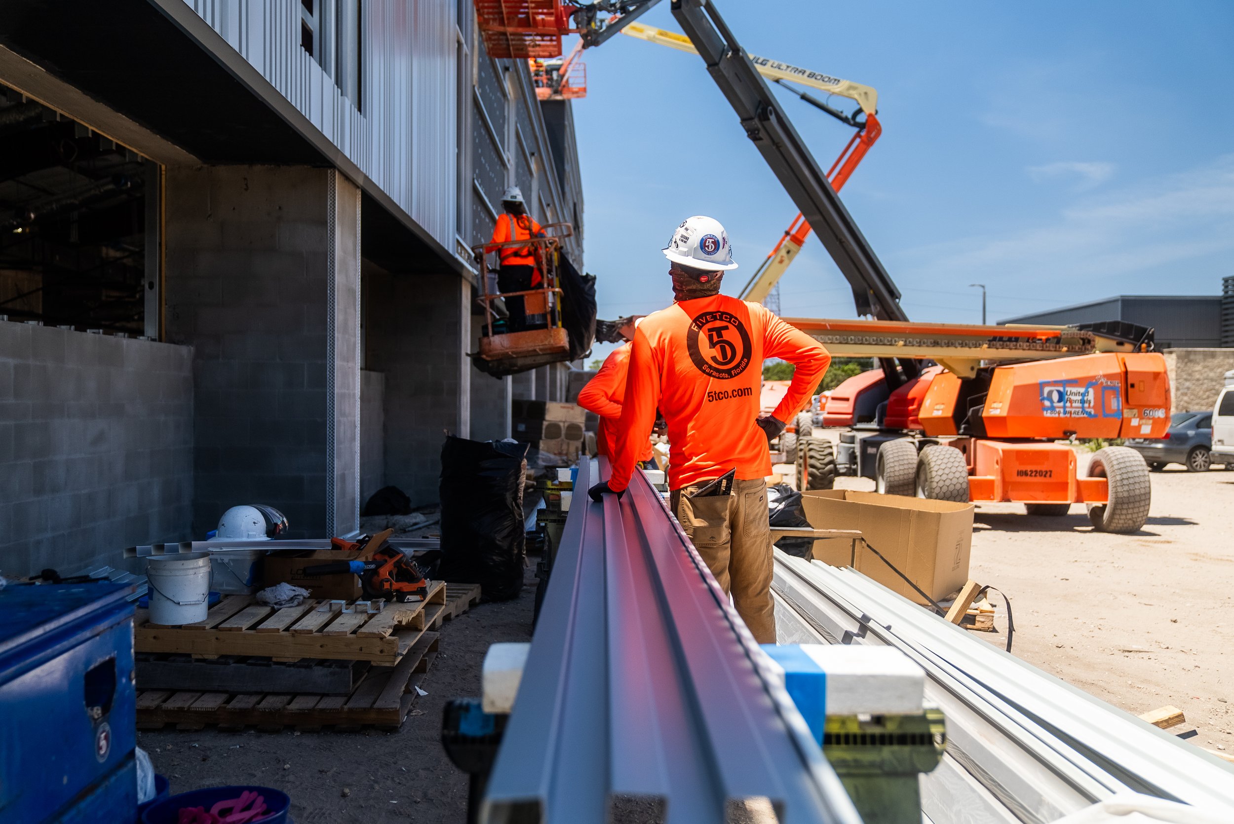 Construction workers in bright orange shirts working on a building site with cranes and other equipment.