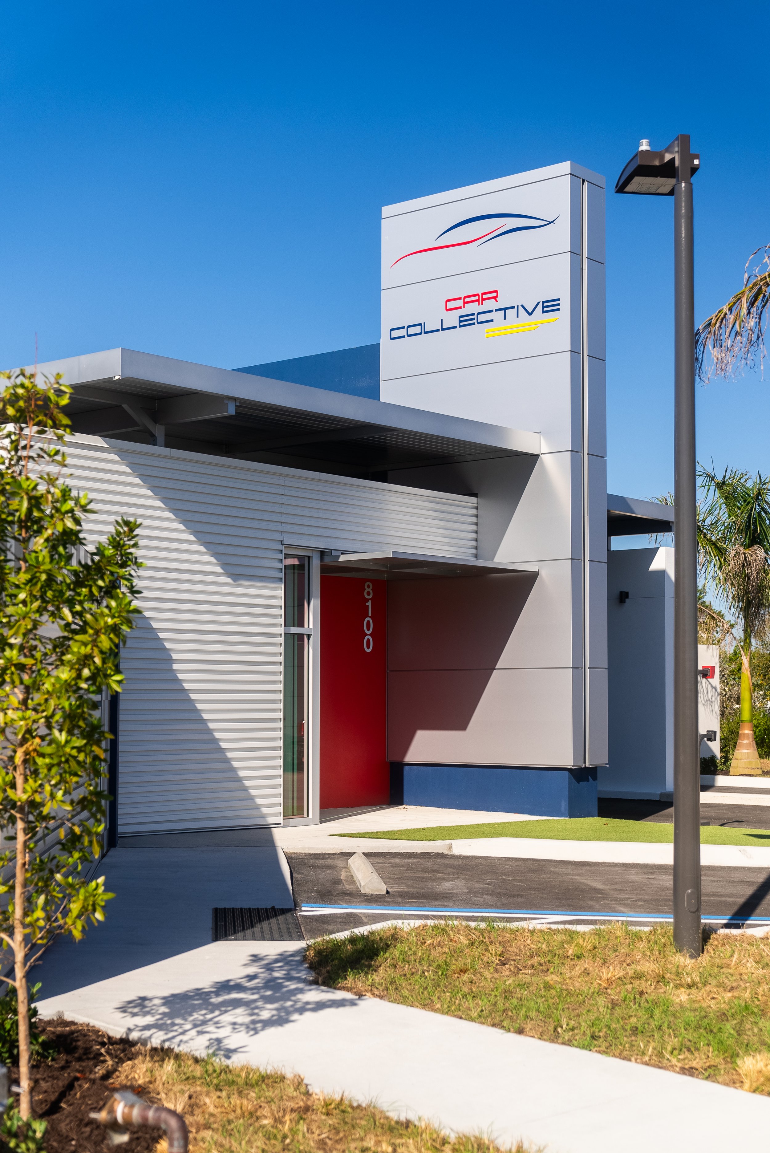 Modern building with "Car Collective" sign, featuring metal siding and a red door, set against a clear blue sky.
