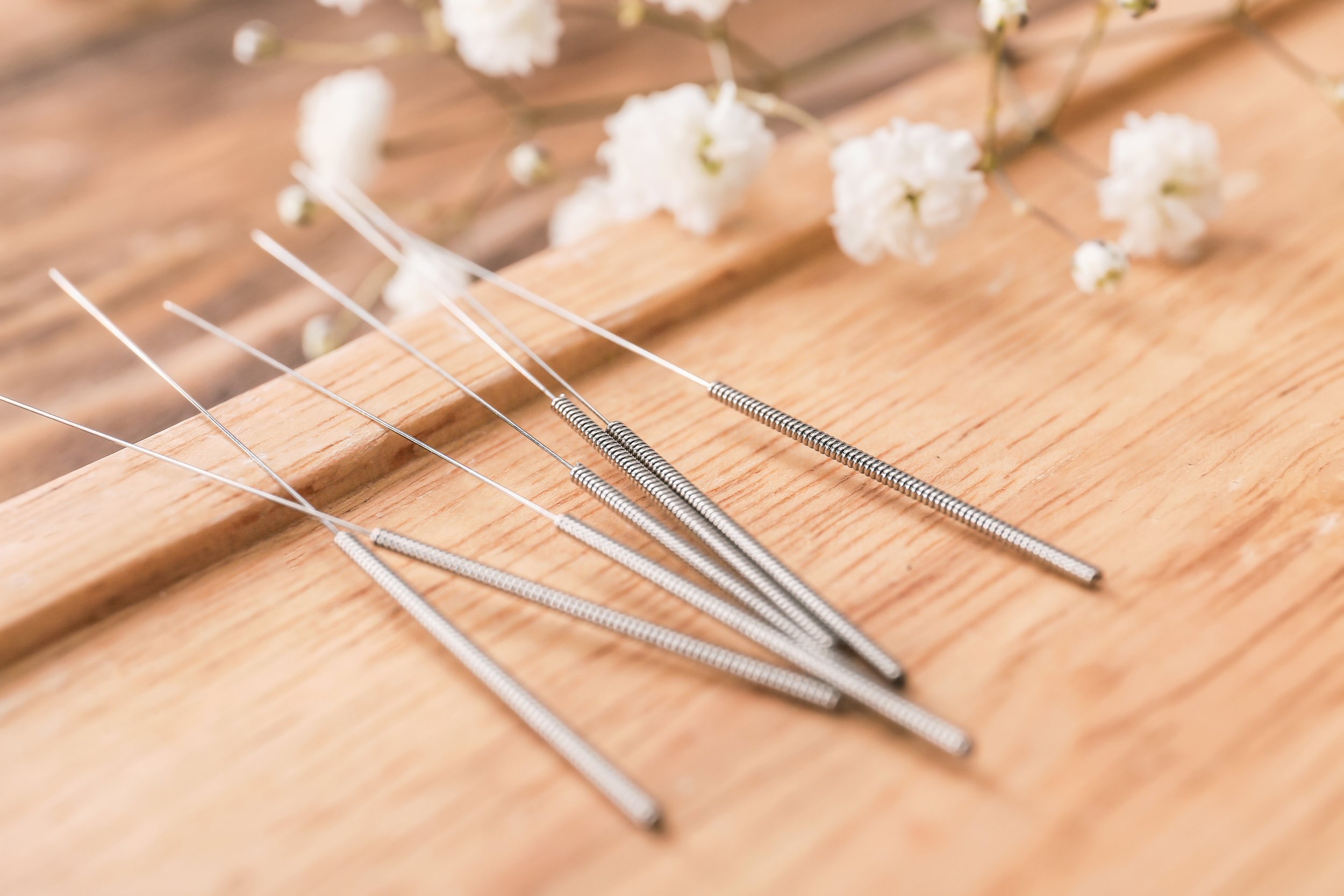 Acupuncture needles on a wooden surface with white flowers in the background.