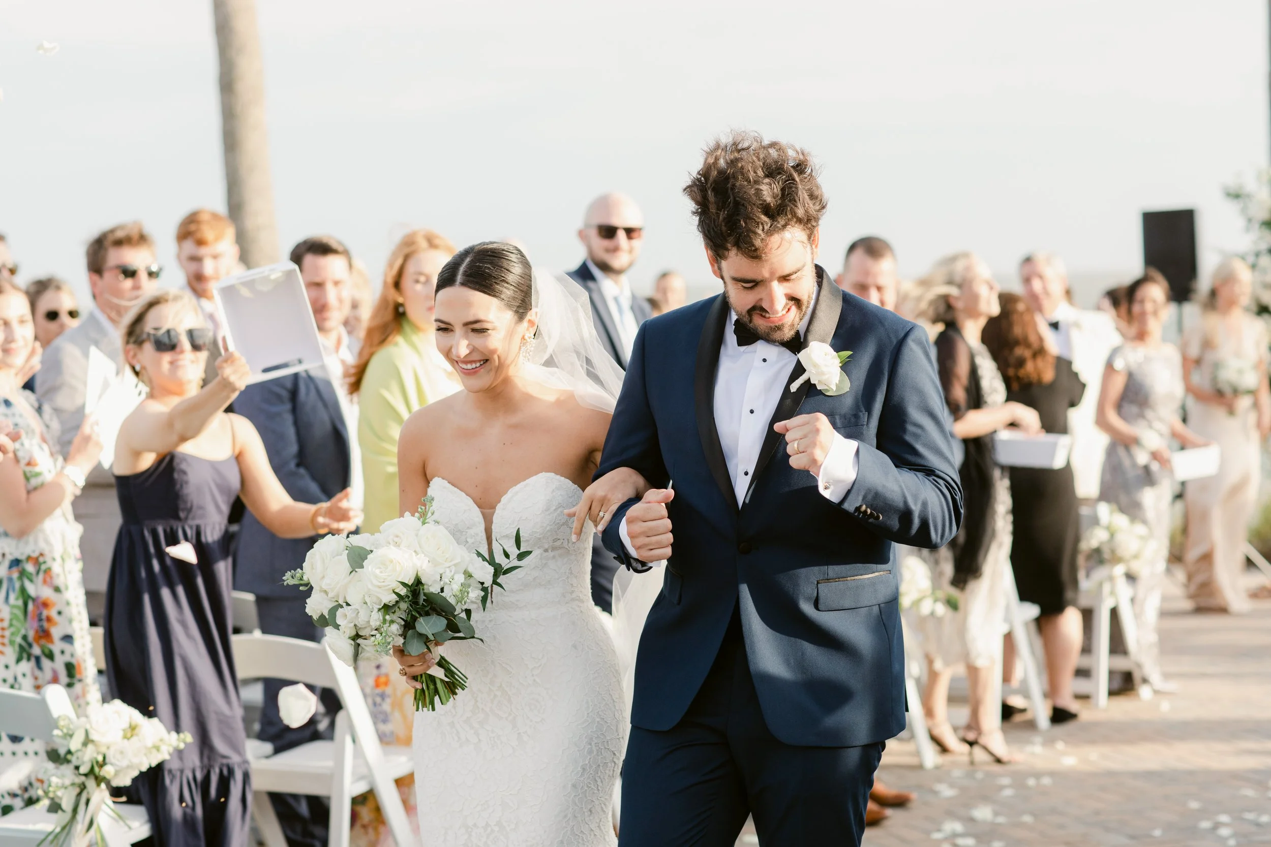 Bride and groom sharing a kiss on grassy coastline at sunset with ocean backdrop — romantic seaside wedding scene.”