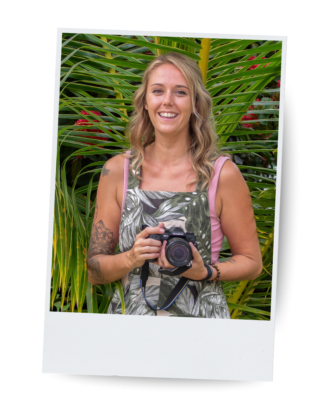 Woman holding camera in front of tropical plants, smiling at camera