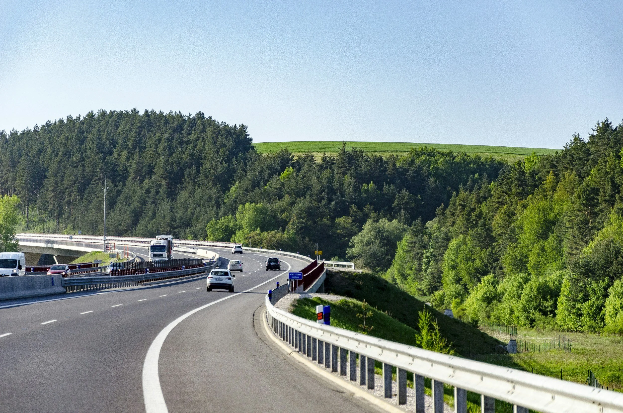 A winding scenic highway with cars driving in both directions through a lush landscape, perfect for a summer road trip.